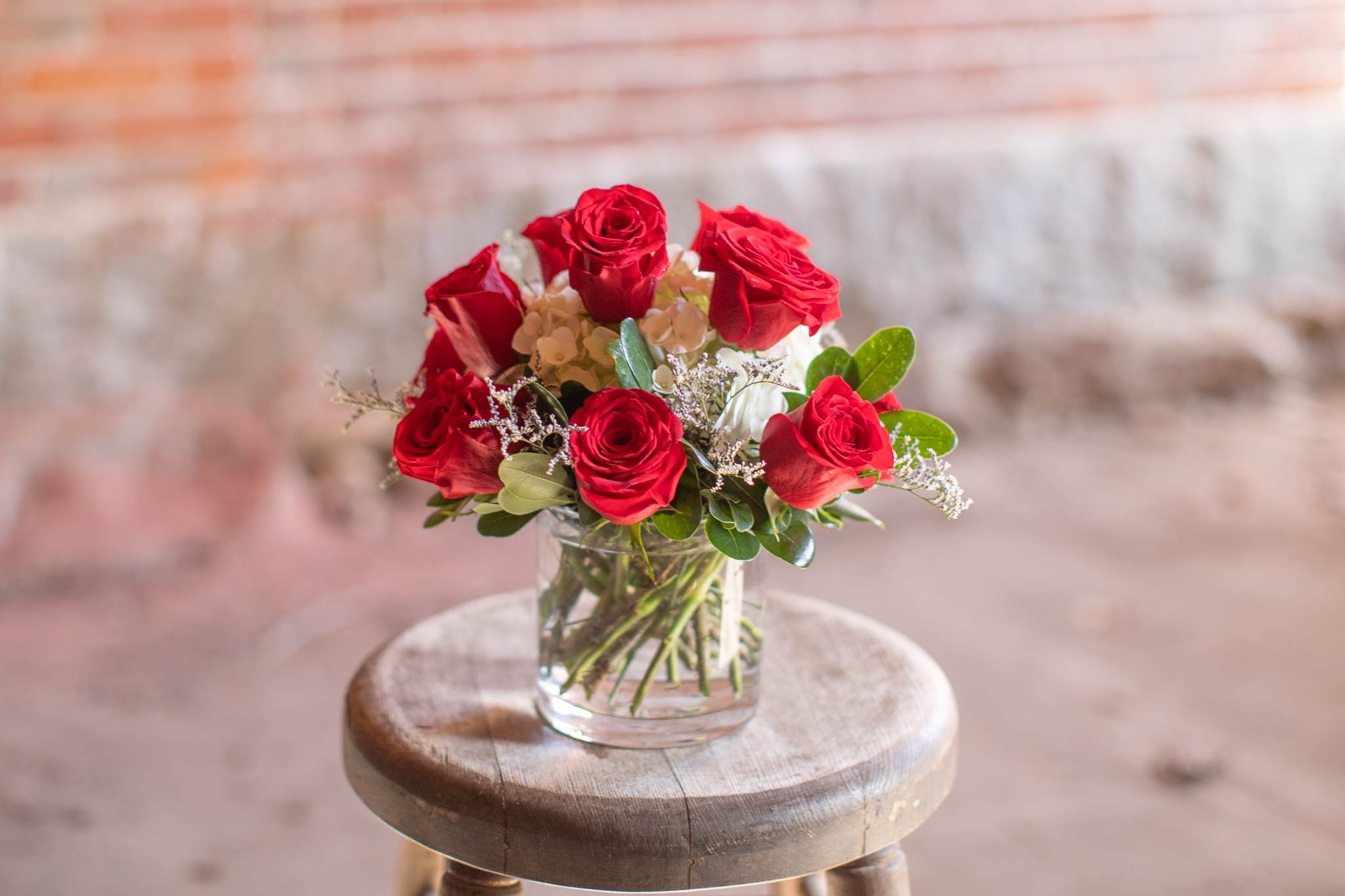 Crimson Compact Dozen - Lovely crimson red roses. Triple A grade premium roses artfully arranged with minimal greenery and hearty hydrangea. This design is perfect for delivery to the workplace so it's easy for your honey to transport home. It's also great for those who are not fans of greenery and all the accent. A simple and elegant take on the timeless dozen. 