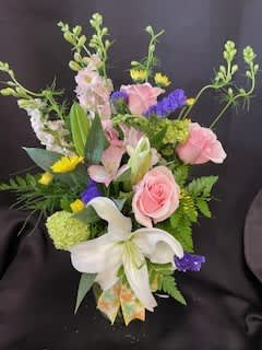 A Mother's Heart - In a clear glass vase, this gorgeous arrangment highlights a white lily surrouded by roses, hydrangeas, crysanthemums, sweatpeas, alstromerias, purple statice in a bed of seasonal greenery with a seasonal bow.