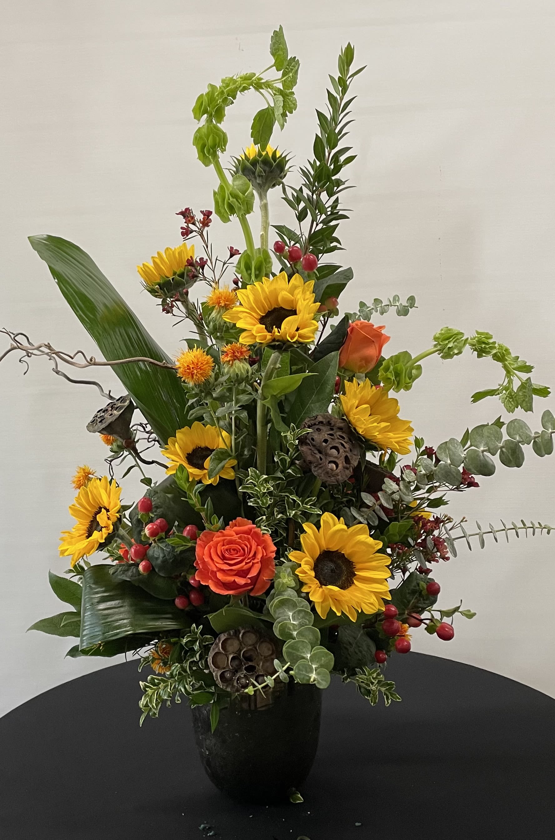 Autumn Contemporary - Sunflowers, Orange Roses, Bells of Ireland and Lotus Pods in a memorable statement.