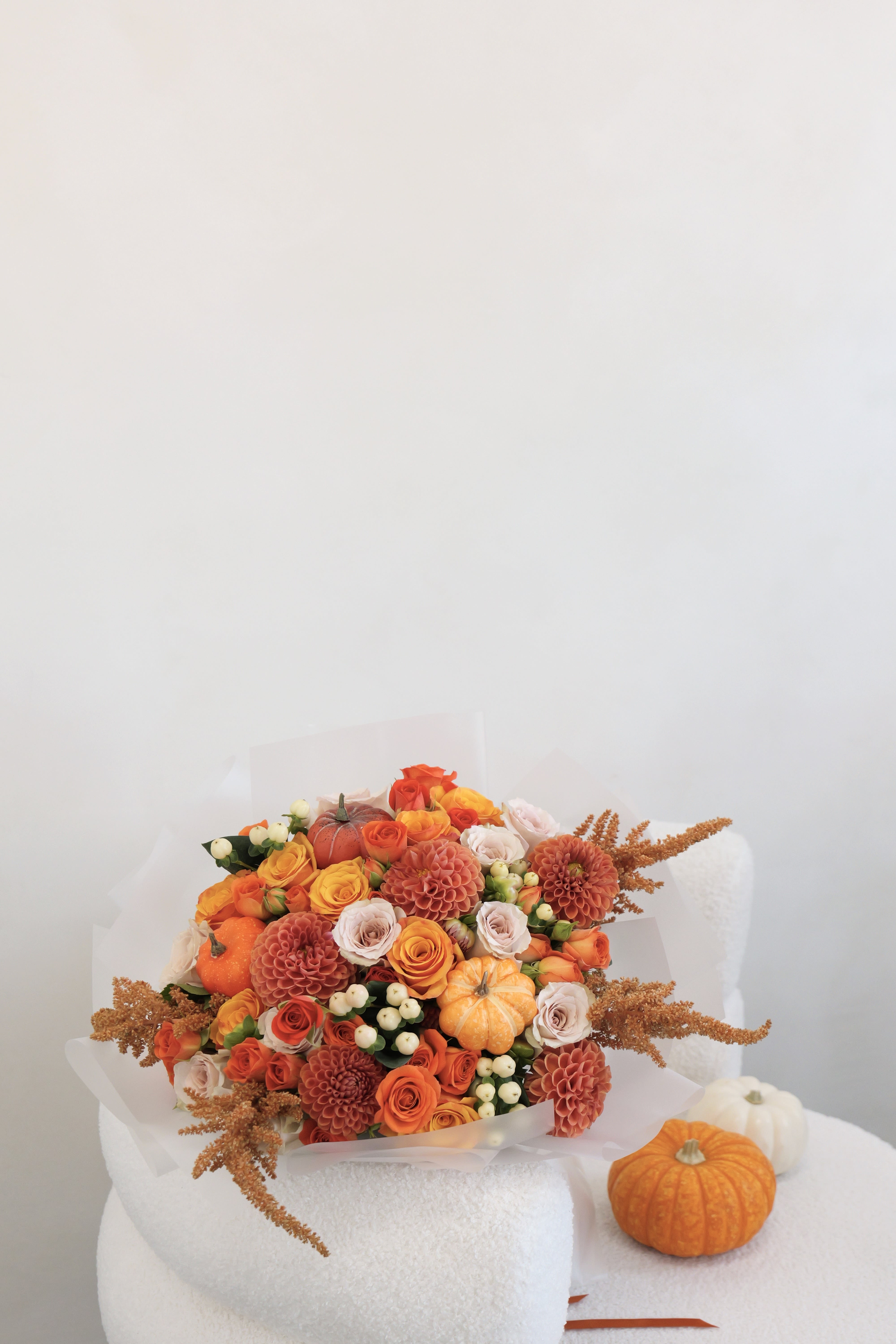 Pumpkin Spice - This bouquet features vibrant orange roses, mini decorative pumpkins, and warm seasonal blooms, wrapped in a clear matte paper, creating a festive and cozy autumn arrangement.