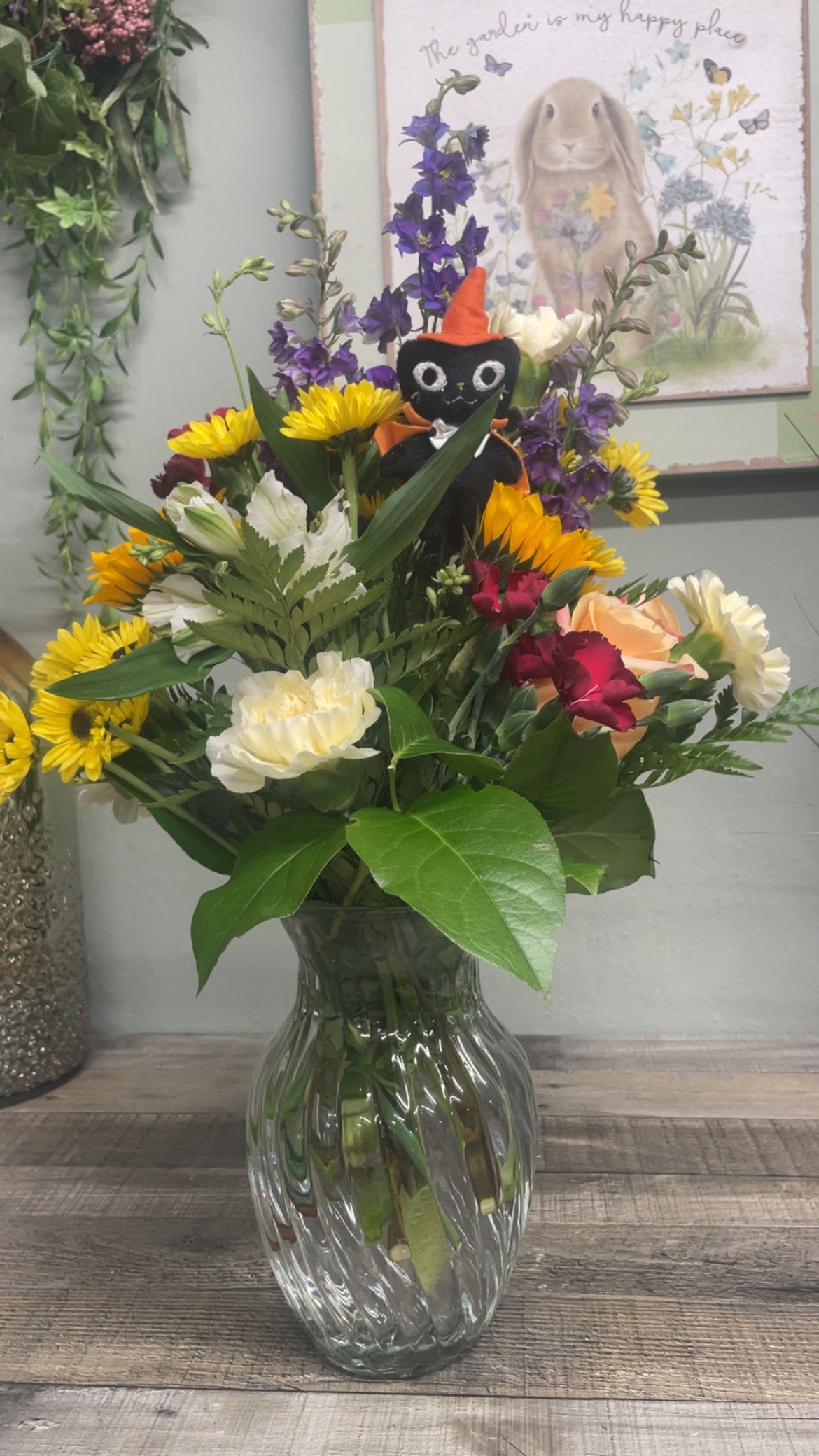 Cat's Meow - A mixed arrangement in a clear glass vase with a Halloween pick added.  When black cats prowl, and pumpkins gleam may luck be yours this Halloween.