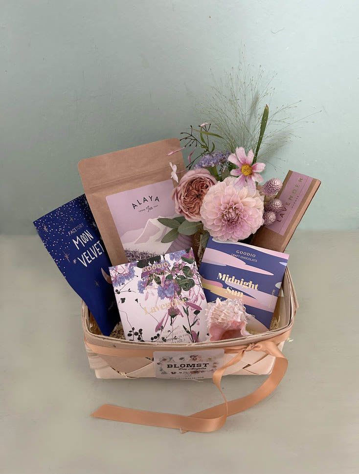Moonlight Basket - Lovely lavender basket packed with pretty goodies and sustainable tea and chocolate. Goodio vegan lavender chocolate (GF): Lavender fields forever - premium craft chocolate topped with fragrant lavender crystals Goodio Midnight Sun white chocolate White chocolate topped with Arctic cloudberry crumble. Nothing shines brighter than the midnight sun. Taste the feeling of endless light! The Finnish company Goodio produces small-batch, “bean-to-bar” vegan chocolate, using the finest cacao beans sourced worldwide.  Alaya Darjeeling Tea: Harvested in the second picking of the year, Darjeeling Second Flush tea comes from the unique terroir of this Himalayan region. Certified organic. Organic and regenerative tea, sourced directly from people and planet-friendly Indian farms. Lavender insence sticks in pretty box Moon Velvet Face Mask Deeply moisturizing sheet mask for dry or combination skin. The sheet mask is formulated to help hydrate the skin, nourish the skin and to help keep the skin’s barrier strong and protected. Mini Blomst arrangement in clear mini vase Shell. Packed in a braded wood basket.   