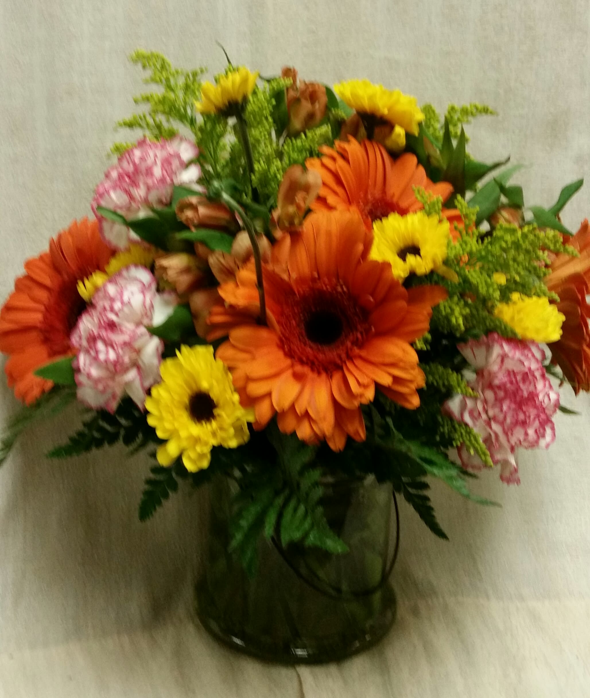 Cheerful Orange gerbera Daisies and More Cheerful Orange gerbera Daisies and More - Clear Cylinder vase with bright and cheerful flowers to include gerbera daises, carnations, pom poms and more!