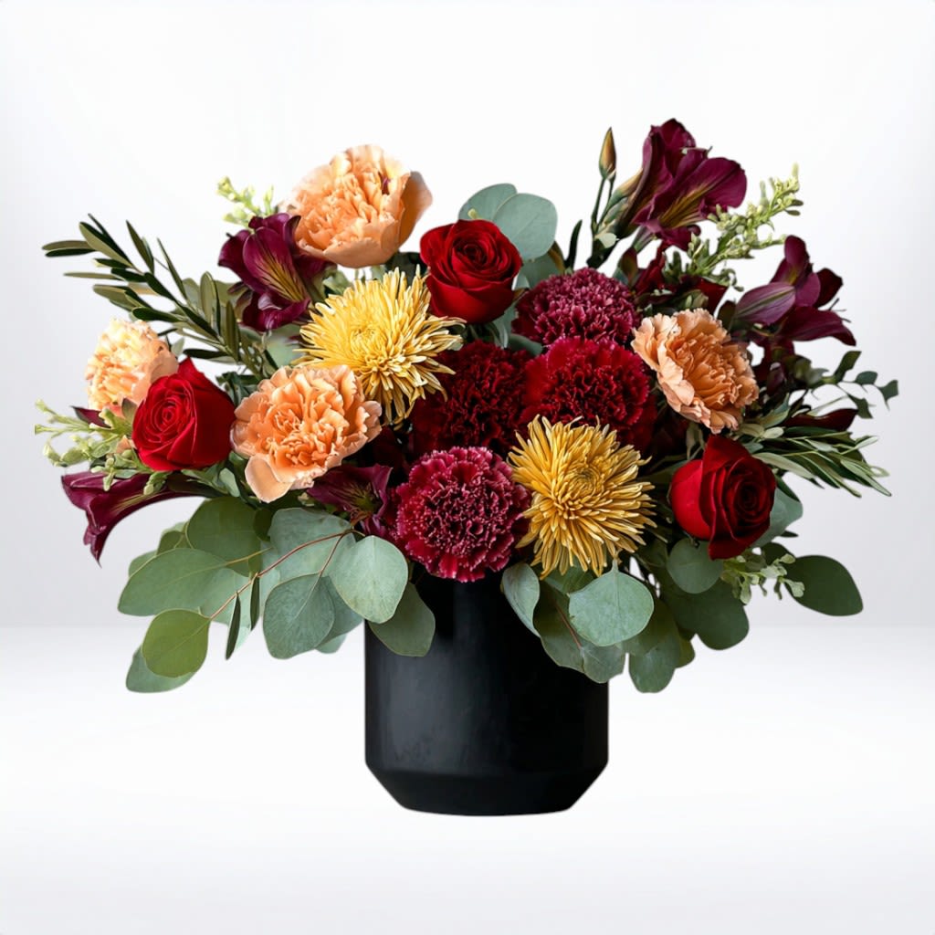Autumn Eclipse - Autumn Eclipse brings together the richness of fall’s most beloved blooms. Featuring deep burgundy mums, fiery orange carnations, radiant golden chrysanthemums, and velvety red roses, this arrangement is designed in a modern matte-black vase for striking contrast. Perfect for autumn birthdays, seasonal décor, heartfelt thank-yous, or sympathy gestures, this bouquet makes a bold yet refined statement.  Available for same-day flower delivery in Galveston, Houston, and surrounding areas, this bouquet brings the spirit of autumn indoors with elegance and charm.  Substitution Disclaimer: Due to seasonal availability, some blooms may be replaced with similar varieties of equal or greater value to maintain the design’s look and integrity. Your arrangement will always reflect the same spirit, palette, and premium quality.