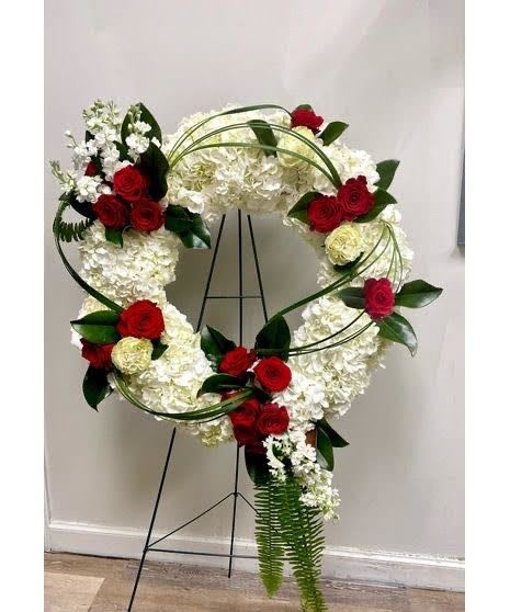 Graceful Remembrance Wreath Graceful Remembrance Wreath - Our Graceful Remembrance Wreath is a timeless tribute designed to honor a cherished life. Featuring a lush base of white hydrangeas accented with elegant red roses and touches of greenery, this standing wreath symbolizes both purity and enduring love. The circular design represents eternity, making it a meaningful expression of sympathy and respect. Perfect for funerals, memorial services, or graveside tributes, this arrangement offers comfort and beauty in a moment of farewell