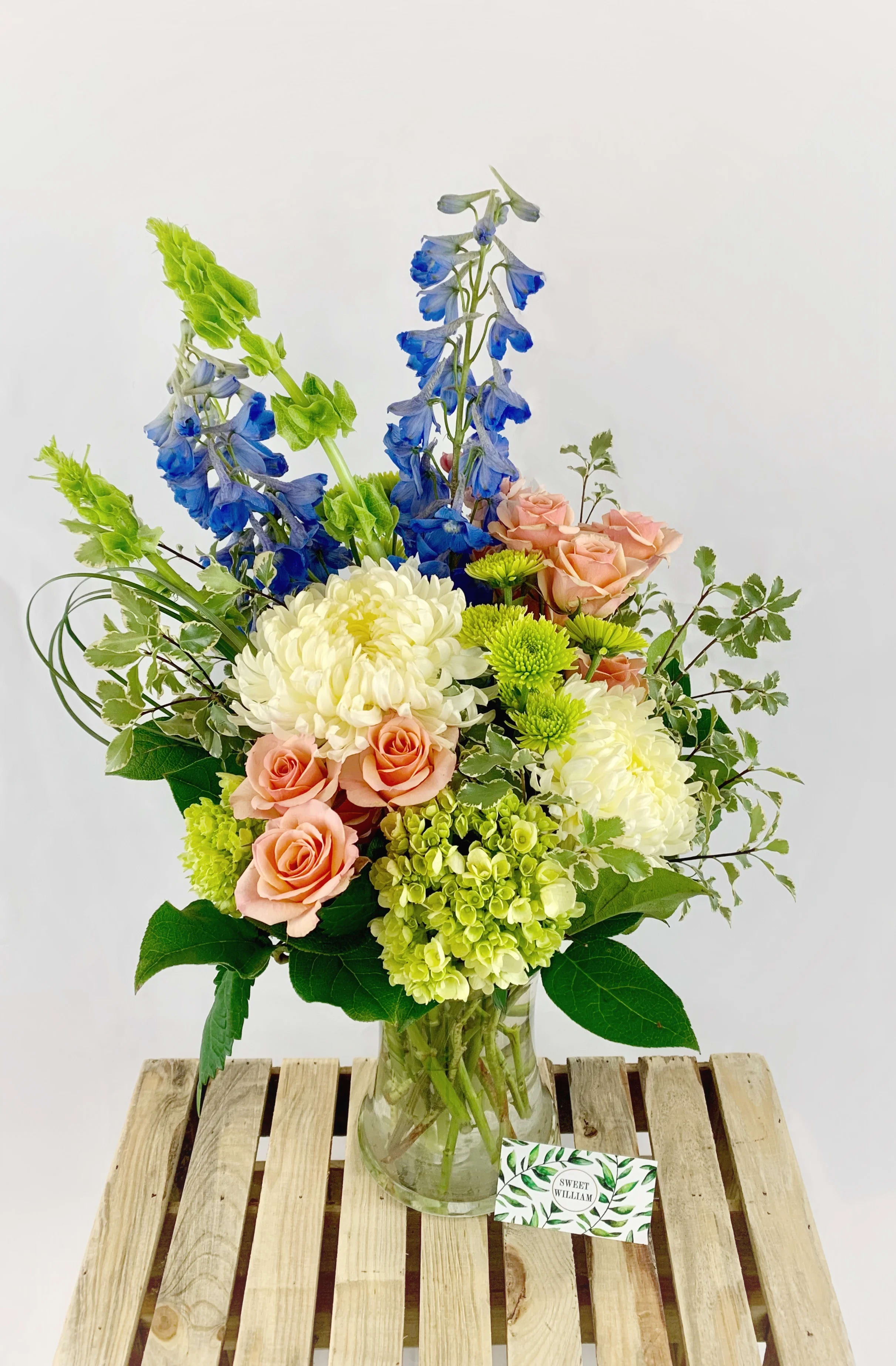 Coastal Breeze Coastal Breeze - A One-Sided Arrangement. Light, refreshing colors reminiscent of a gentle coastal breeze. With peach spray roses, light green hydrangea, football chrysanthemums, light blue delphinium, and green button poms. Stands approximately 17" tall and 12" wide. Please Note: Standard Delivery for this product occurs in the afternoon, between 2:30pm and 7pm. If you need it by a certain time, there is an option to select a timed window for scheduled deliveries.