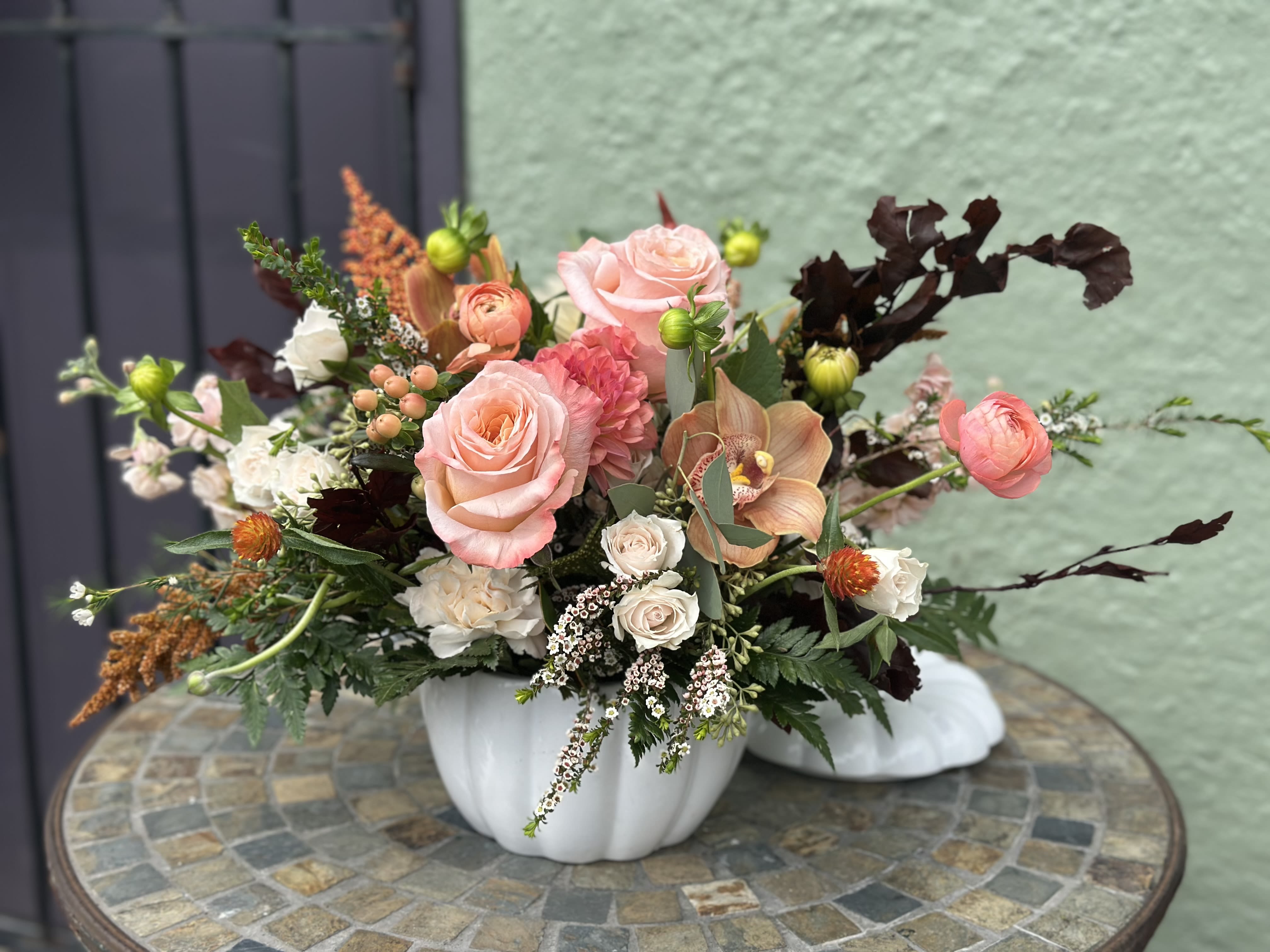 Harvest Moon - &quot;Harvest Moon&quot; is a lush seasonal arrangement brimming with autumn warmth and elegance. Nestled in a white pumpkin vessel, it features a radiant mixt of garden roses, ranunculus, orchids, and textured blooms in shades of peach, coral, and cream, accented with rich foliage and seasonal berries. Perfect for a falll gathering, a frestive centerpiece, or a heartfelt gift, this design captures the magic of autumn evenings under a glowing harvest moon.