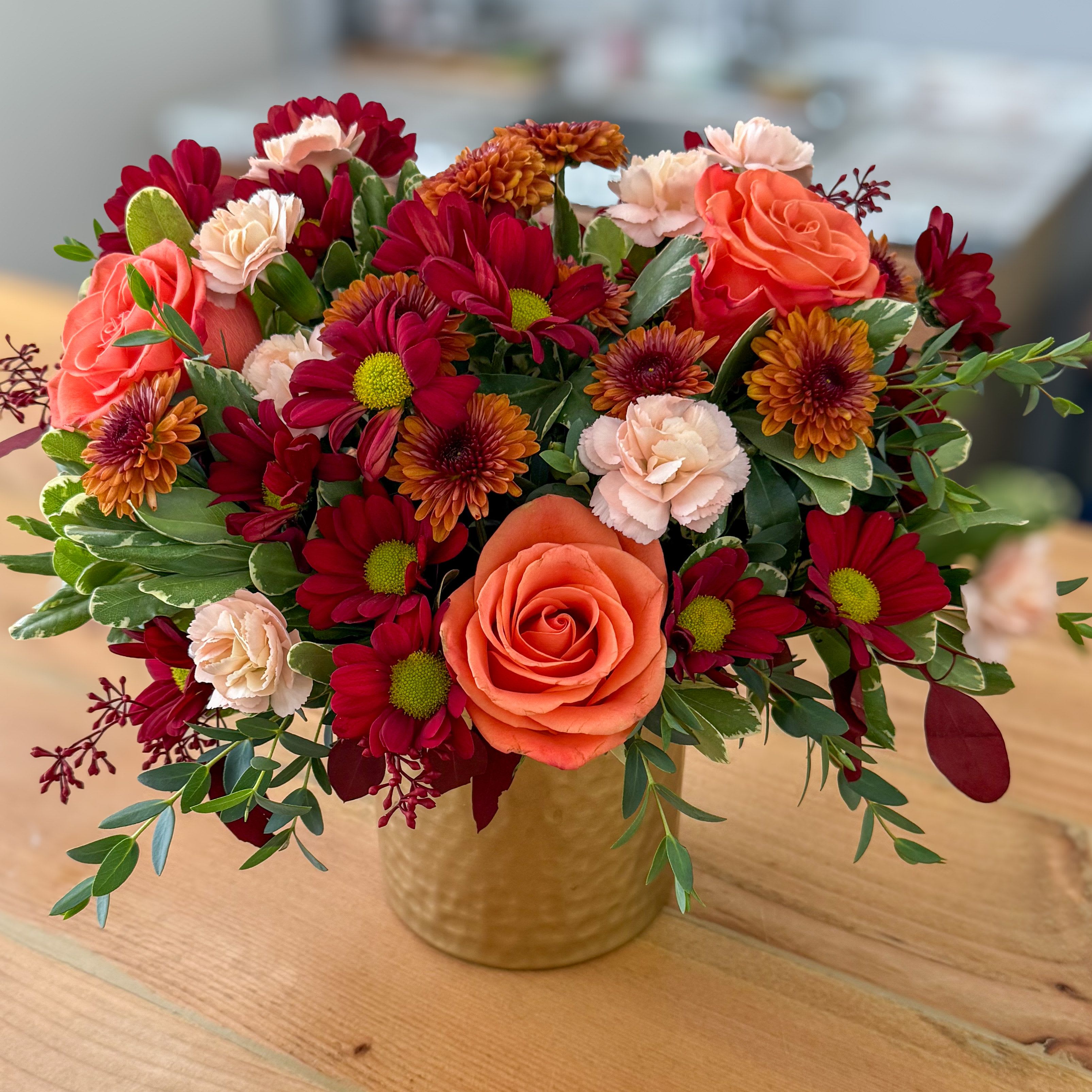 Spiced Cider - A cheerful mix of orange roses, mums, and soft blush blooms in a gold vase — a warm and cozy arrangement for any fall occasion.