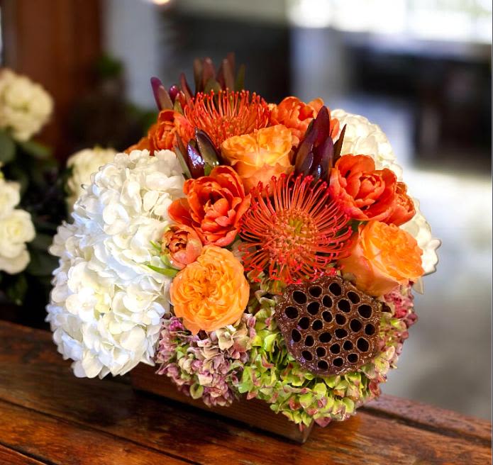 A Desert Sunrise  A Desert Sunrise  - This design includes both White and Green Antique Hydrangeas, Pincushion Protea, Roses, Tulips, Safari Leucadendron, and Lotus Pod set in a dark wood container. This design measures approx. 12"W x 12"H. Please check with our office for availability before placing orders online.