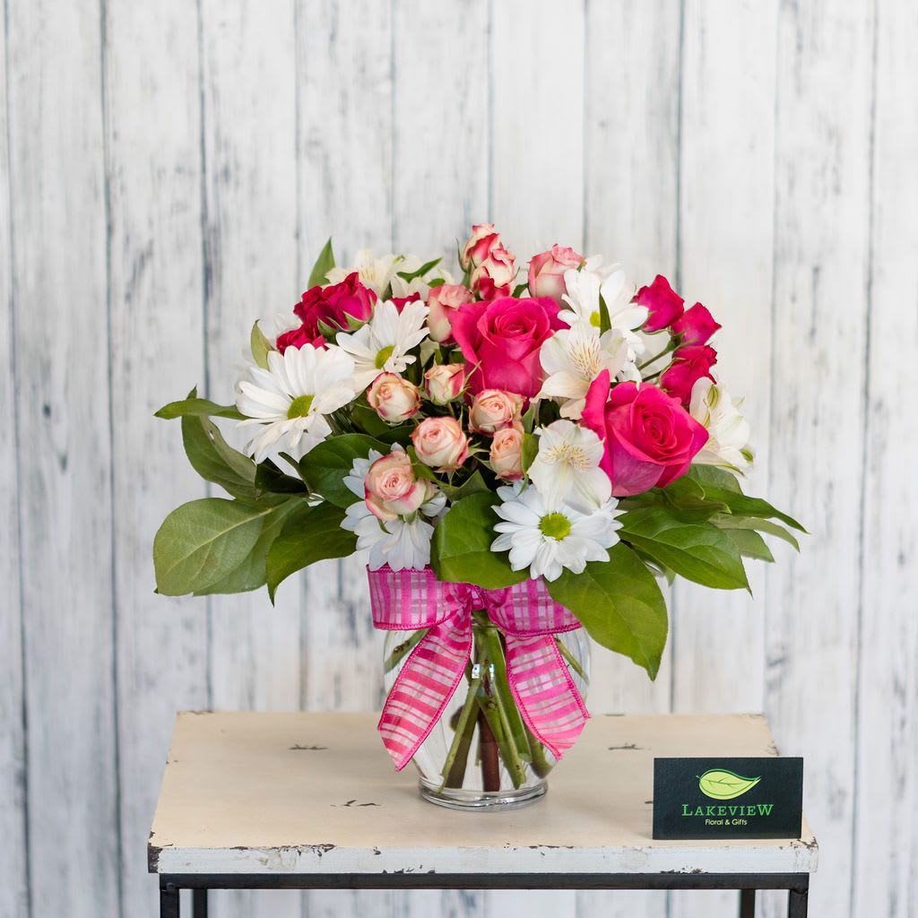 Frolic Frolic - Whimsical and bright~ a classic vase is filled with long lasting daisies accented by pink roses and spray roses. Polka dot ribbon adds the finishing touch! Approximate Dimensions: 10" H X 8" W
