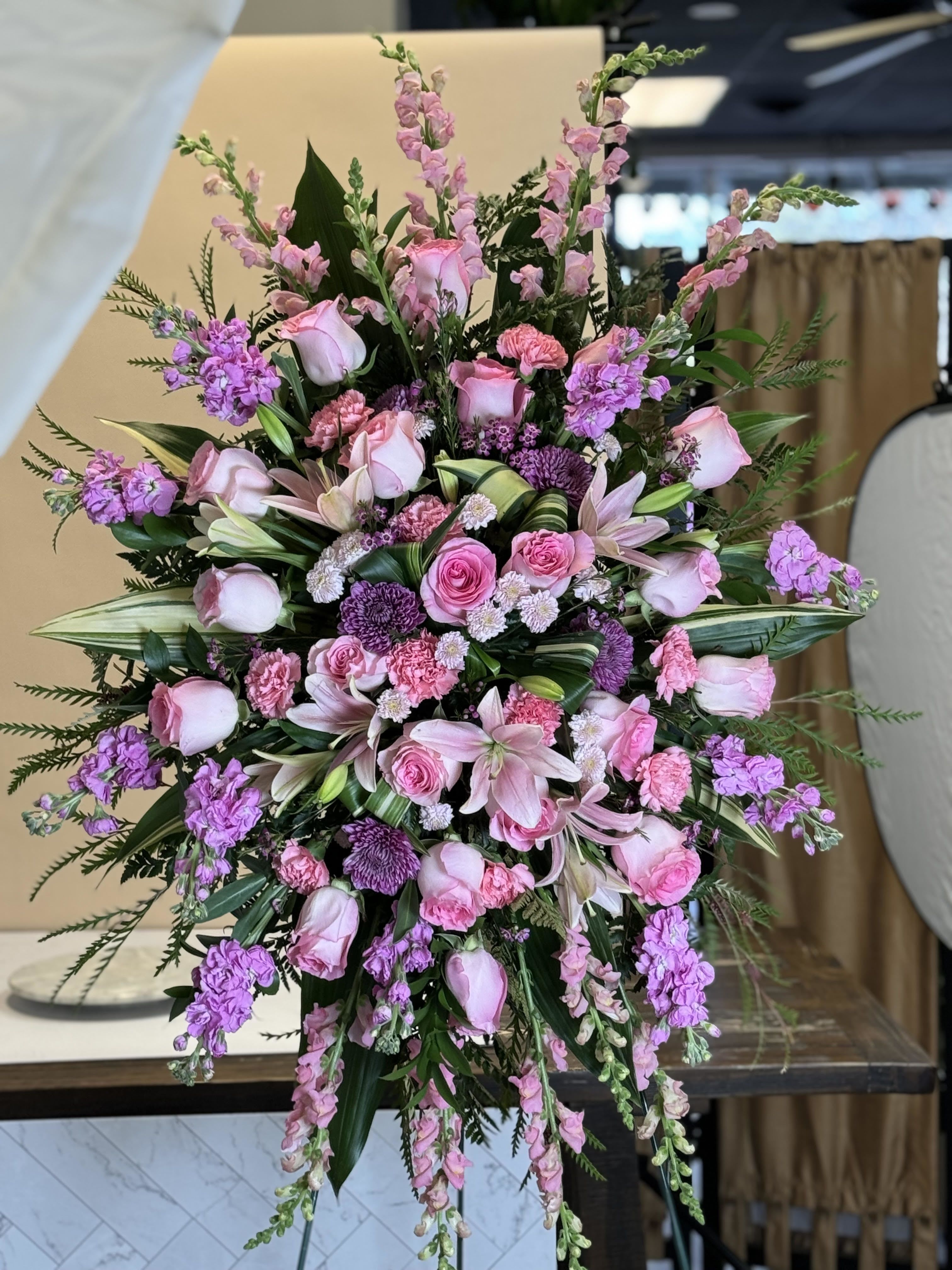 Pink Tribute Spray - A graceful expression of love and remembrance, this standing spray is designed with shades of soft pink blooms. Featuring roses, snapdragons or stock, mums, lilies, and carnations, complemented by fresh greenery, it creates a tender tribute filled with warmth and beauty.