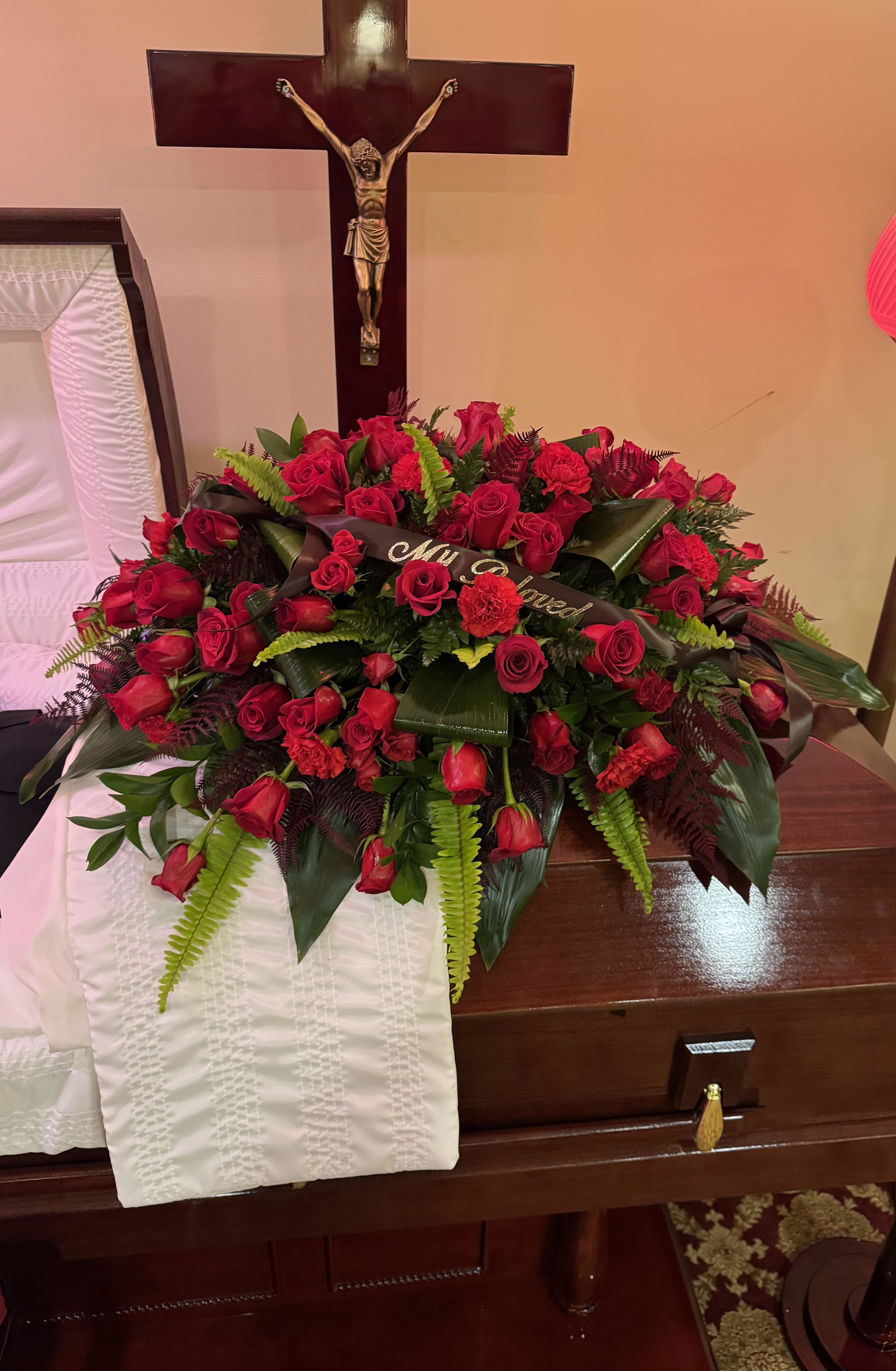 Eternal Love Casket Spray - A heartfelt tribute designed with deep red roses, spray roses, and carnations, gracefully accented with lush greenery. This is a timeless symbol of love, respect, and remembrance.