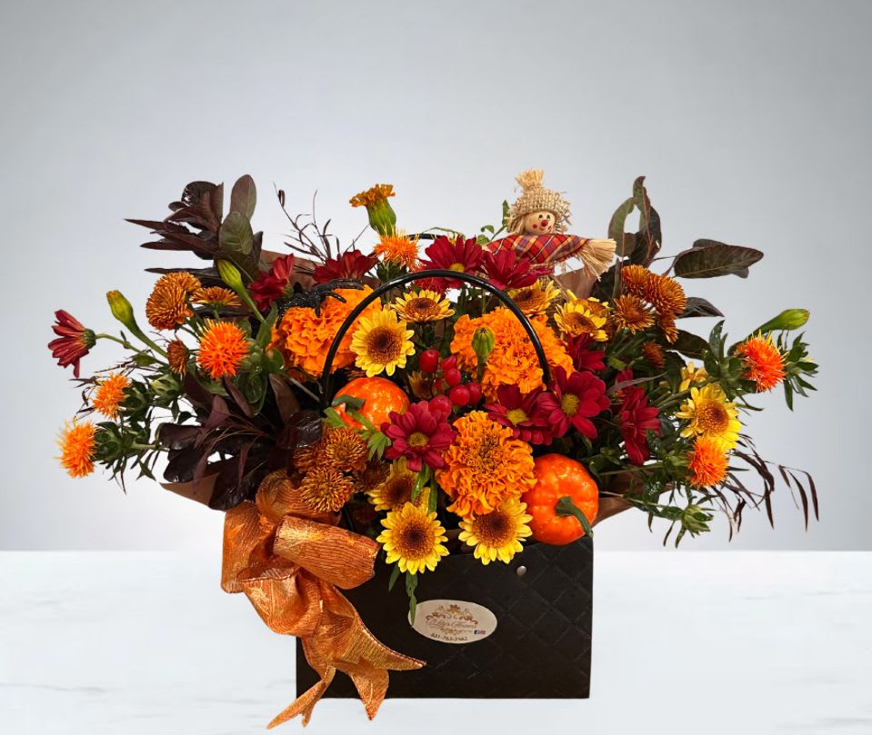 Autumns Purse - A festive fall arrangement made in a little purse filled with vibrant blooms, mini artificial pumpkins, and a cheerful scarecrow—perfect for adding a touch of autumn charm to any space.