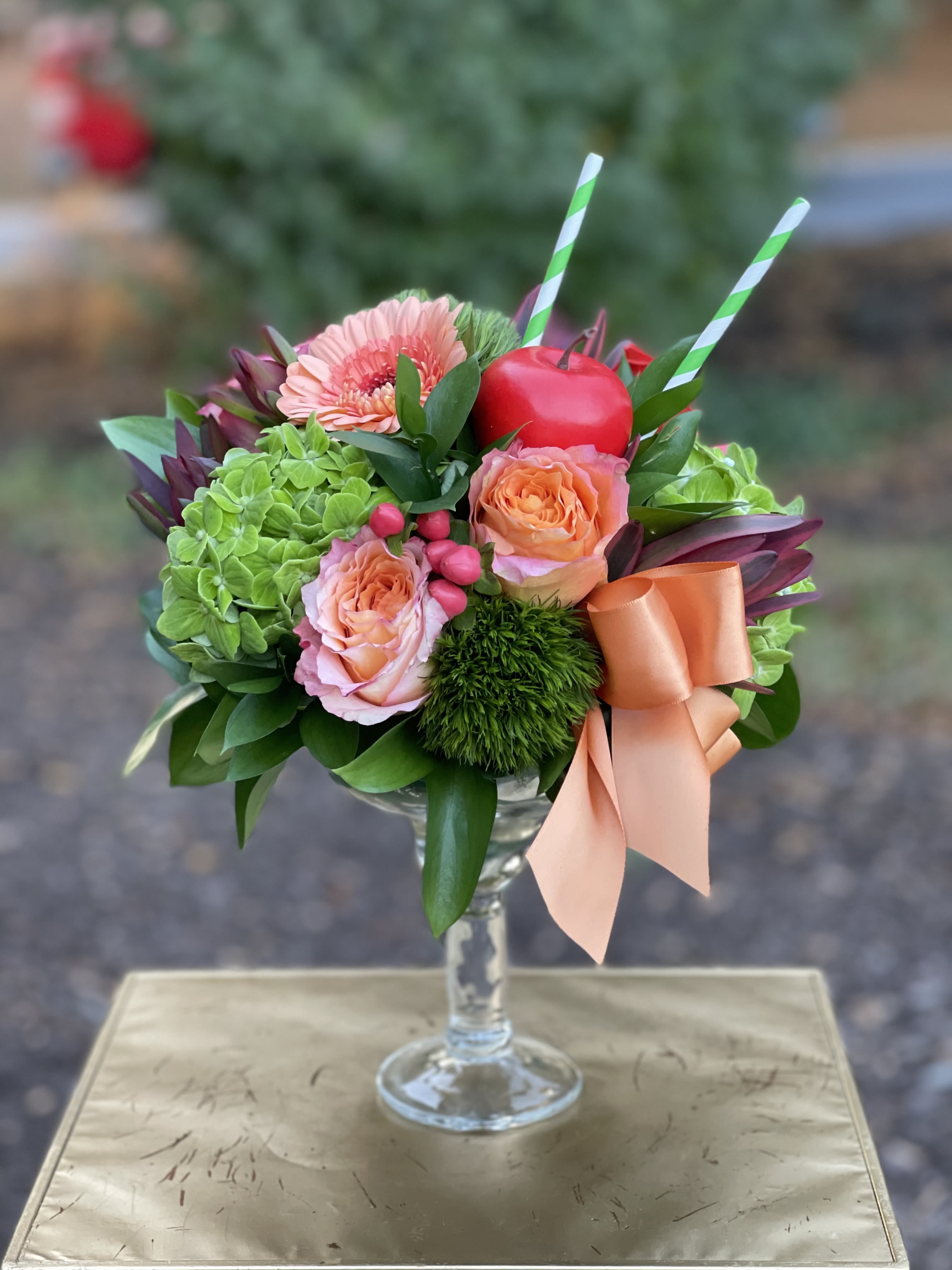 Appletini Appletini - Appletini | Wilmington, Delaware Florist Shake up the season with Appletini, a playful and vibrant floral arrangement handcrafted by Petals Flowers and Fine Gifts in Wilmington, Delaware. This unique cocktail-inspired design features bold orange roses, lush green hydrangea, textured green trichilium, a striking orange gerber daisy, and exotic protea. Finished with a faux apple, straws, and a peach satin ribbon, all styled in a sleek martini glass, Appletini is the perfect blend of creativity and charm. Ideal for birthdays, celebrations, dinner parties, or as a standout gift, Appletini brings a touch of fun and sophistication to any setting. Its mix of bold colors, unique textures, and whimsical details makes it a conversation starter and a stylish addition to home or office décor. As your trusted local florist in Wilmington, Delaware, Petals Flowers and Fine Gifts specializes in luxury floral designs created with premium blooms and artistic flair. We proudly offer same-day, tax-free flower delivery throughout Wilmington, Hockessin, Newark, Chadds Ford, Glen Mills, Kennett Square, and nearby communities, ensuring your flowers arrive fresh, beautiful, and ready to impress. We offer custom floral designs with unique, premium flowers. We are a family-owned Wilmington, Delaware florist with personal, reliable service. Same-day, tax-free flower delivery.