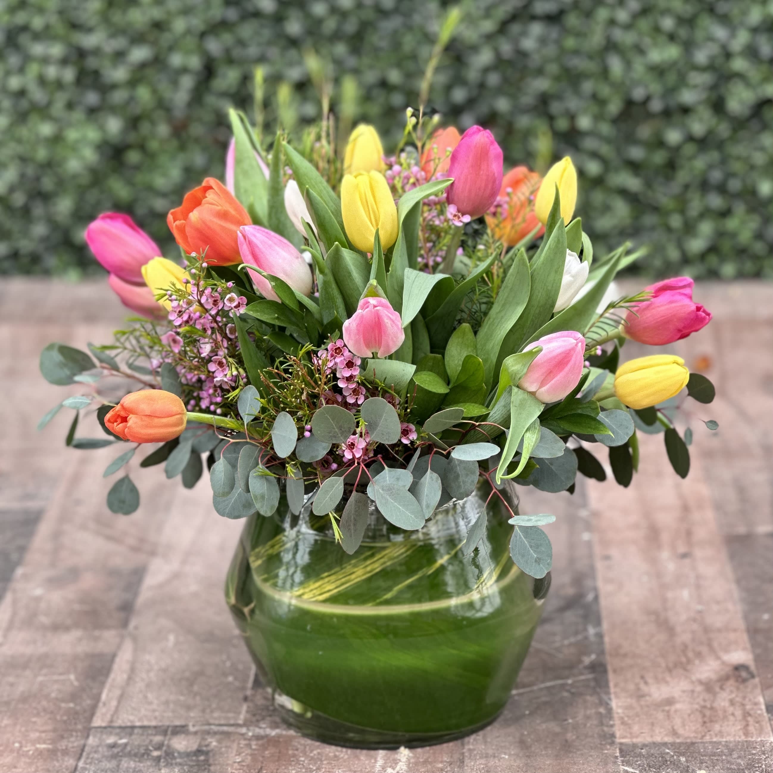 A WALK IN THE TULIP FIELD - A colorful assortment of tulips in a glass vase with greens and filler. 