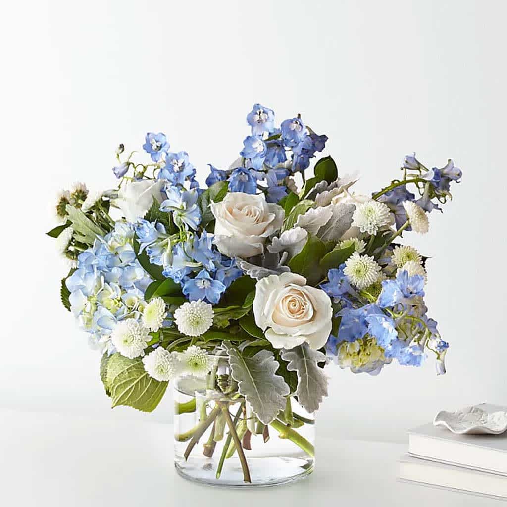 Clear Skies Bouquet - Clear Skies Bouquet is a serene and cool-hued bouquet, this arrangement showcases the soothing tones of blue and white.   With delicate blue hydrangeas, soft white roses, and accents of lighter blues, it's elegantly arranged in a clear vase.  Approximately 16&quot;H x 20&quot; W.   