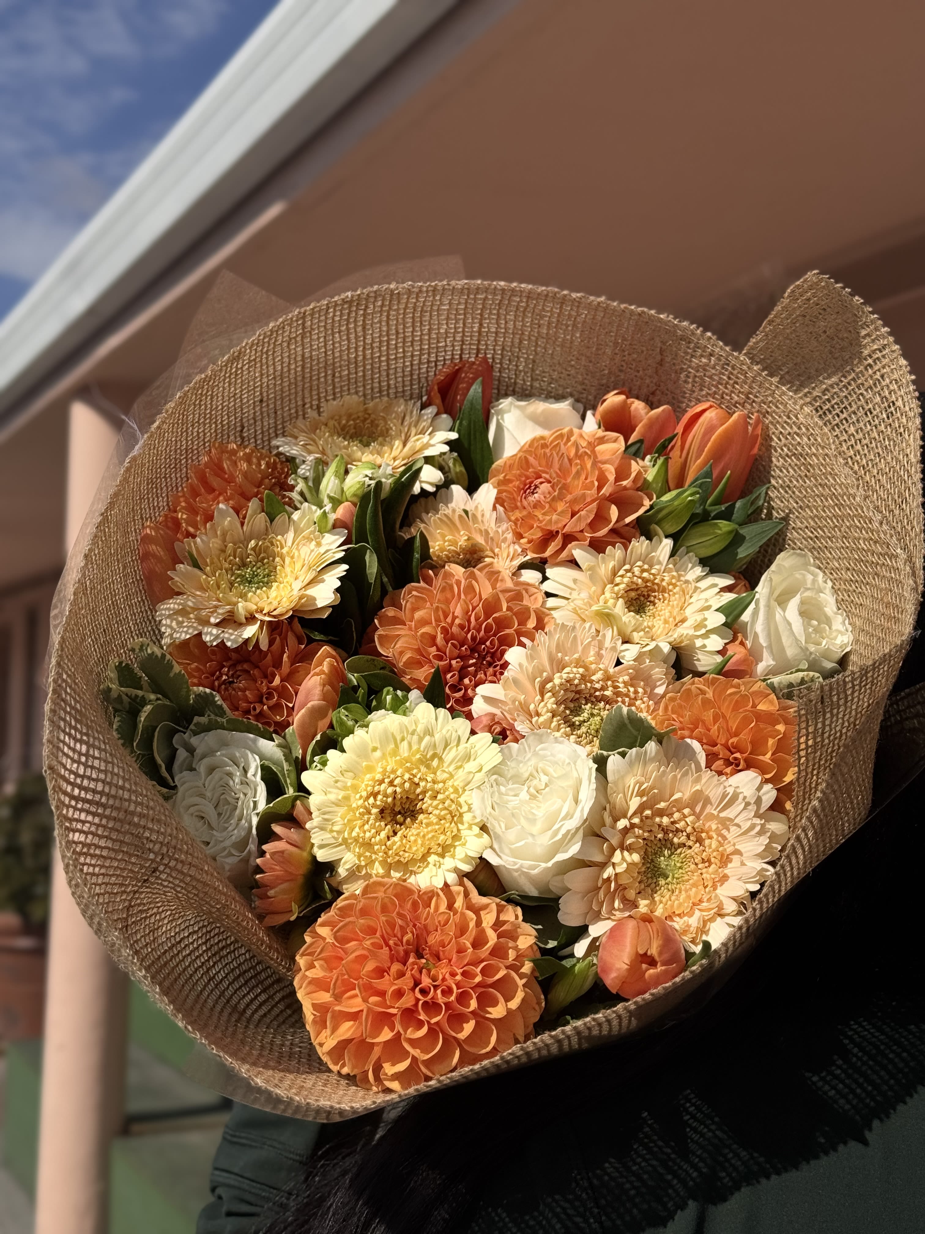 Rustic Autumn Charm - Our Rustic Autumn Charm bouquet is the perfect balance of elegance and warmth. Wrapped in natural burlap for a cozy, rustic touch, this hand-tied bouquet features a rich mix of creamy white roses, golden gerberas, burnt-orange dahlias, and soft peach blooms. The layered textures and autumn tones make it an unforgettable piece full of seasonal beauty.