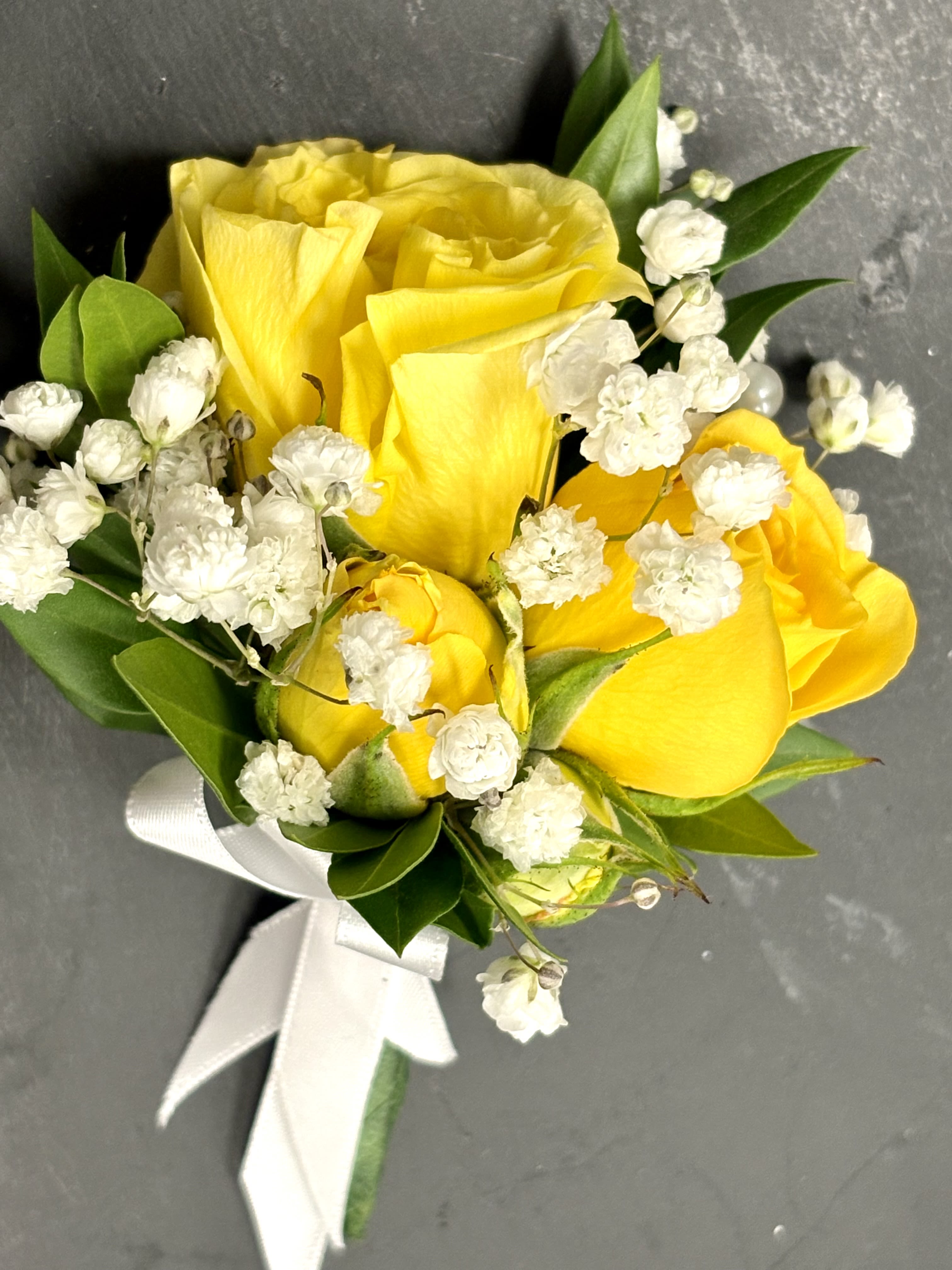 Sunny Delight Boutonniere By VLM Flowers - Cheerful yellow roses accented with soft baby’s breath and fresh greenery, tied together with a crisp white ribbon.