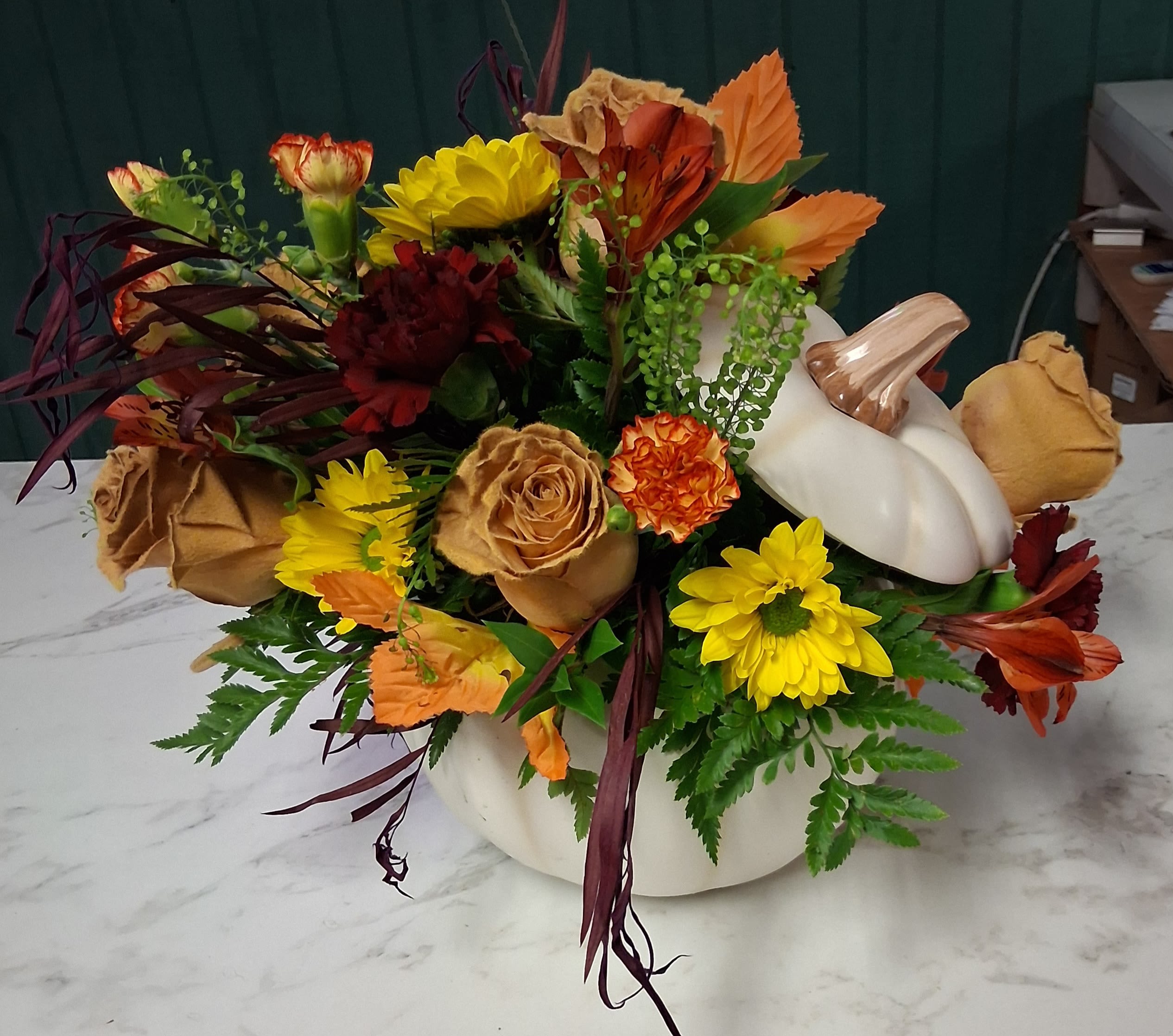 Pumpkin Promenade - Bring the beauty of fall indoors with our Pumpkin Promenade, thoughtfully designed in a charming white pumpkin container. Each piece is one-of-a-kind, filled with a random assortment of autumn flowers such as roses, mums, carnations, and other long lasting seasonal flowers and greenery. A perfect gift for the season—or a cozy touch for your own home!   Please Note: No two arrangements are exactly alike. If you have requests for specific flowers, kindly include them in the special notes section at checkout.