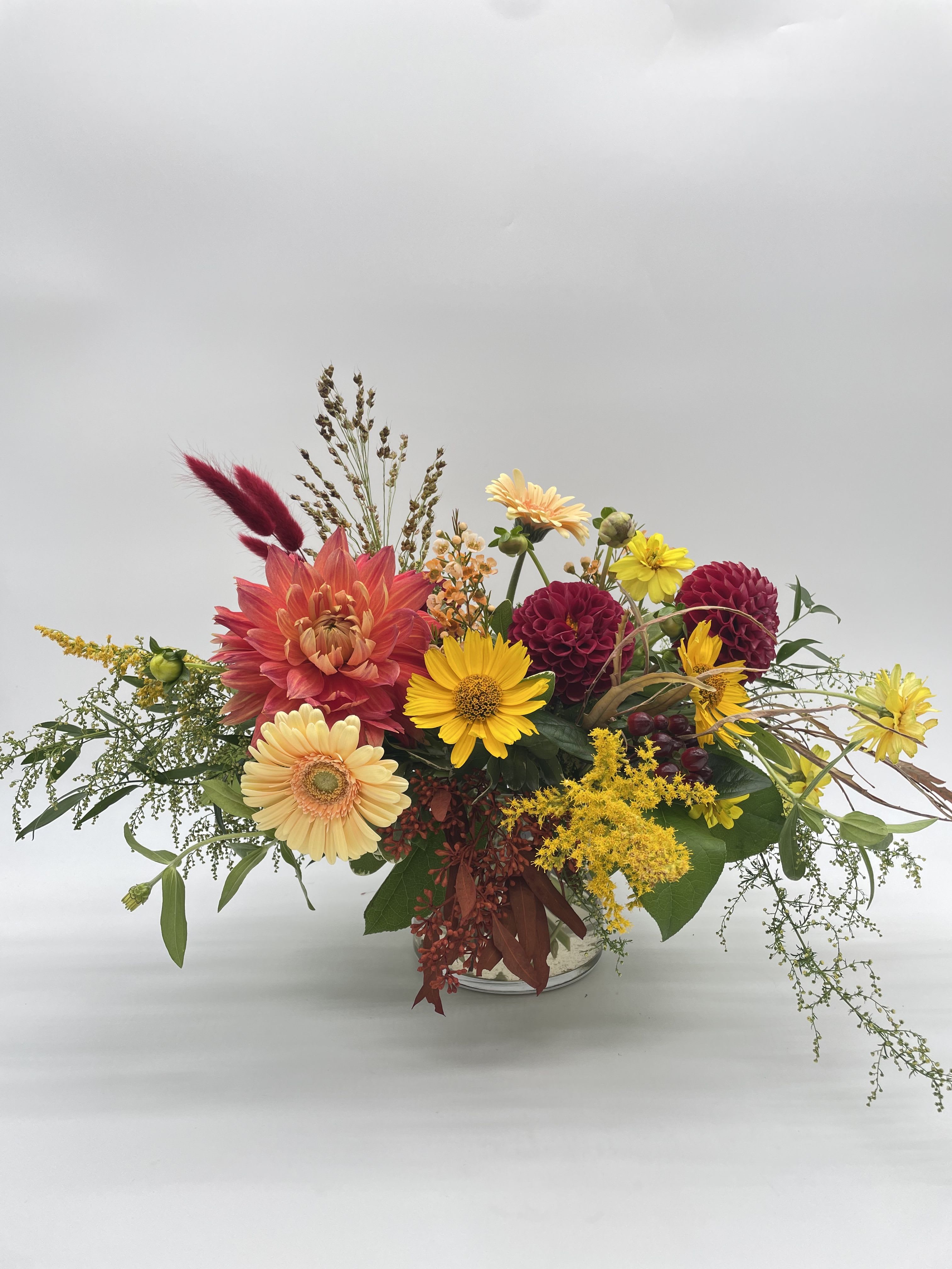 Crisp and Cozy Harvest Crisp and Cozy Harvest - Low and lush, colorful seasonal arrangement created in a 5 x 5 clear cylinder vase. A fall look made up of a balanced mix of shades of burgundy, peach, and vibrant yellows with textured greenery and filler. This arrangement is seasonal and available while a majority of supplies last. Designers may need to implement substitutions, however will follow the general arrangement style and color theme. Standard price point is pictured.