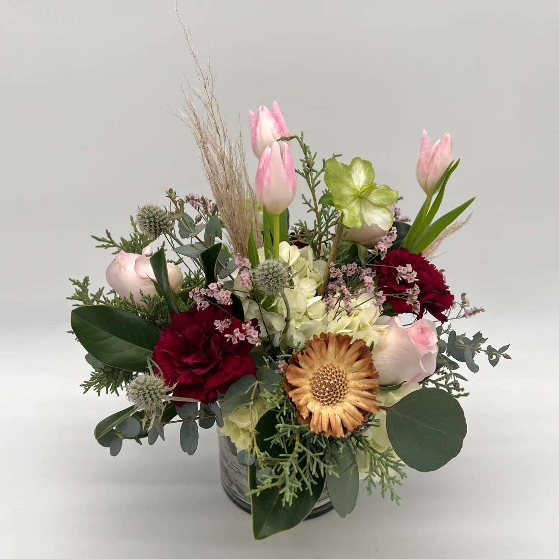 Birch and Blush - Florist original low and lush arrangement in a birch-lined 5x5 vase. Beautiful boho and winter mix with tulips, hydrangea, roses, winter greens and wood accents. Designers may need to implement substitutions, however will follow the general arrangement style and color theme. Standard price point is pictured.  Bloom Details Hydrangea Rose Tulip Carnation Waxflower