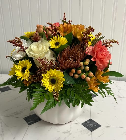Sweater Weather - Capture the cozy charm of autumn with this elegant arrangement designed in a white ceramic pumpkin. Featuring muted fall tones of warm creams, soft oranges, golden yellows, and lush greenery, it’s a seasonal favorite that feels just like your favorite knit sweater—inviting, comforting, and effortlessly stylish. Ideal as a fall centerpiece or a thoughtful seasonal gift.