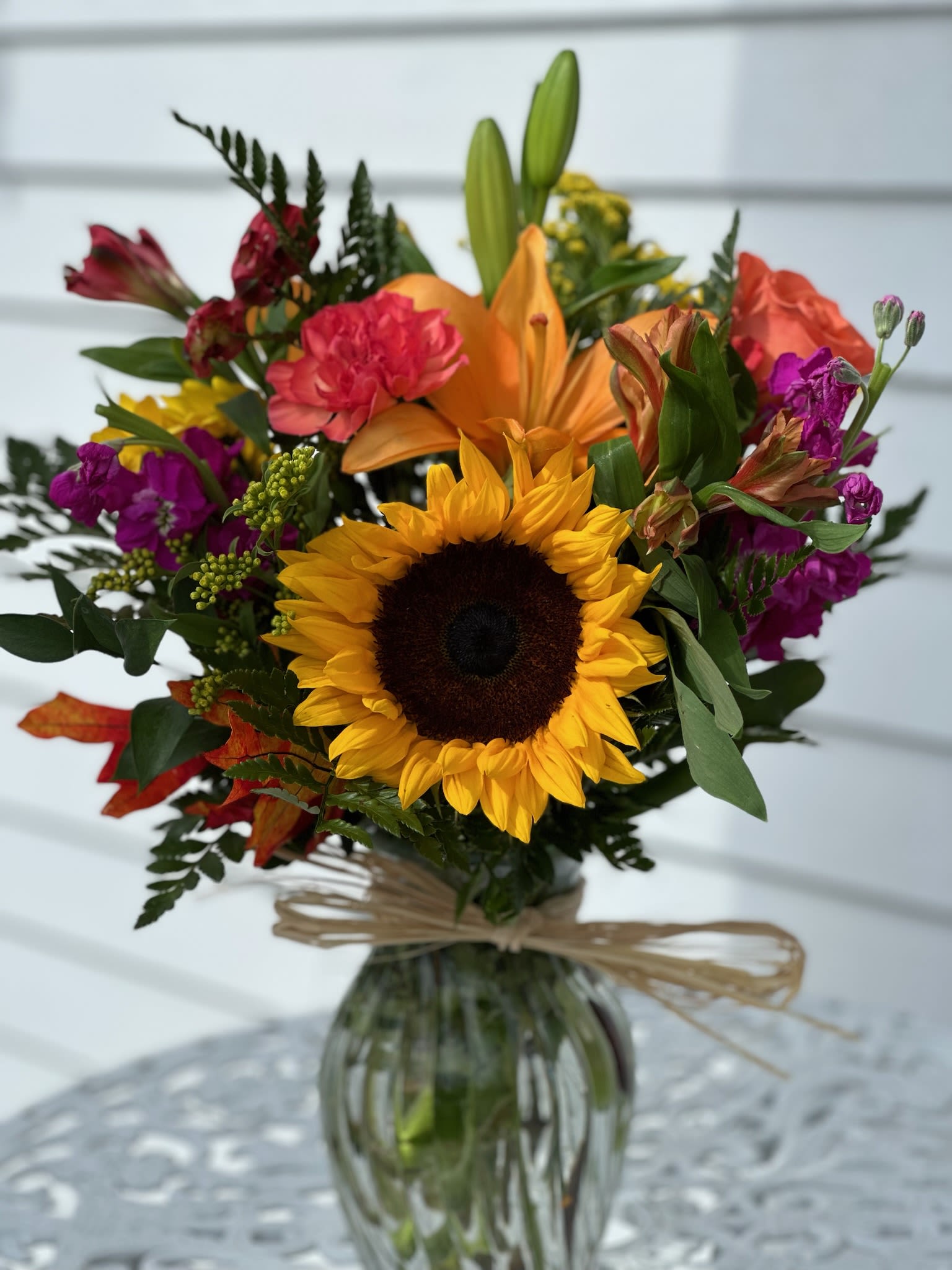  Fall Brilliance Bouquet - Sunflowers, Orange Lily, orange roses carnations, magenta stock alstro and faux leaves arranged in a vase