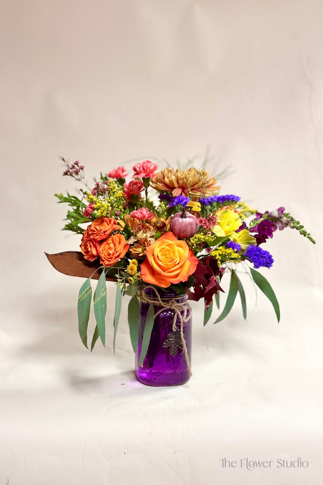 Give Thanks Give Thanks - This vibrant arrangement captures the warmth and richness of the fall season. Designed in a striking purple mason jar tied with rustic twine, it features a delightful mix of orange roses, golden mums, burgundy accents, and pops of bright yellow and purple blooms. Eucalyptus and seasonal greenery add natural texture, while a charming mini pumpkin detail makes it perfect for fall celebrations. A wonderful gift for Thanksgiving, autumn birthdays, or simply bringing a touch of seasonal beauty into your home. Our artists hand-design each arrangement, so Flowers & Containers colors and style may vary due to local availability therefore we are unable to fulfill any requests for specific florals, colors, or containers/vessels.