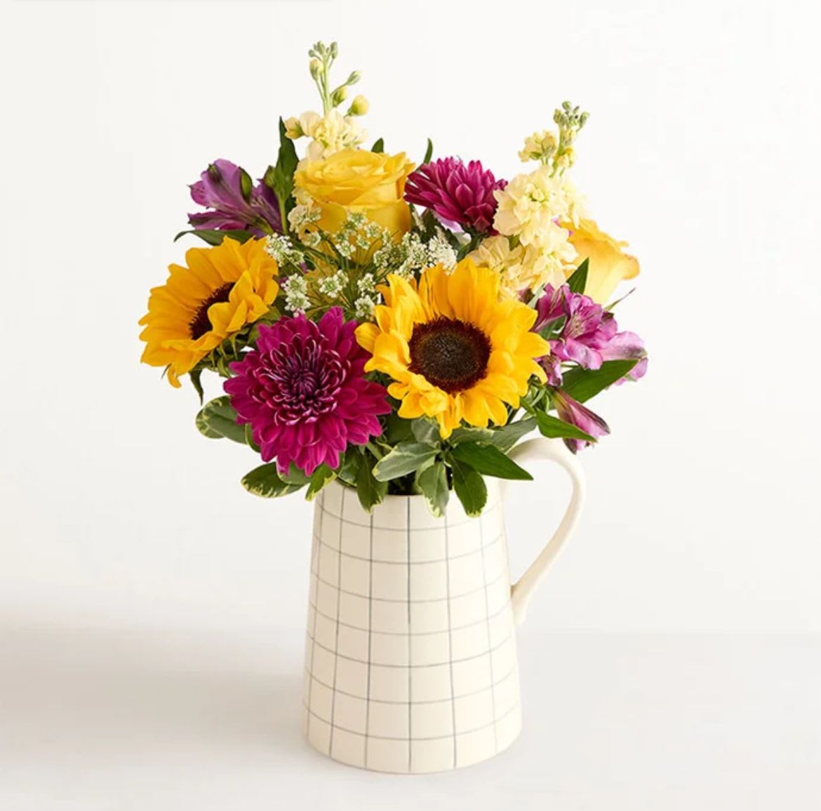 Golden Violet Harmony - Make someone’s day a lot brighter with this mixed arrangement in a charming ceramic vase. Roses, sunflowers, Peruvian lilies, and more in a lively, lovely palette burst forth from a pitcher-shape vase decorated with a windowpane plaid motif. It’s a pick-me-up they’ll long remember.
