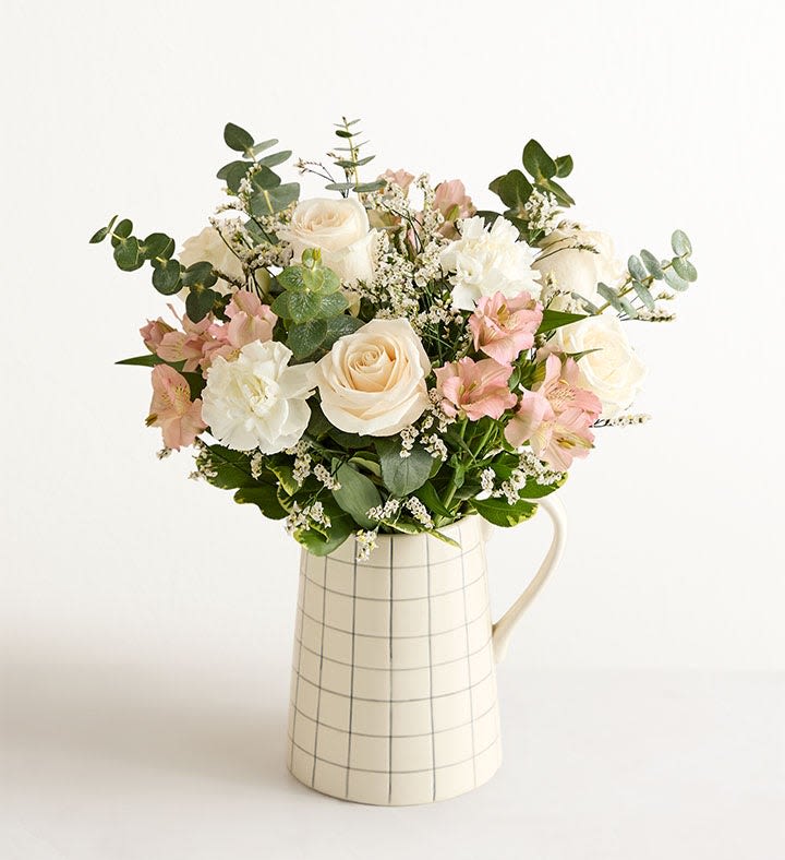 Natural Elegance Bouquet - This is a luscious gathering of roses, Peruvian lilies, and other blooms in white and peach tones, accented with shapely greenery. The bouquet is arranged by hand in our pitcher-shape ceramic vase, which only adds to its charm. Large arrangement measures approximately 16”H x 12”W Medium arrangement measures approximately 15”H x 11”W Small arrangement measures approximately 14”H x 10”W