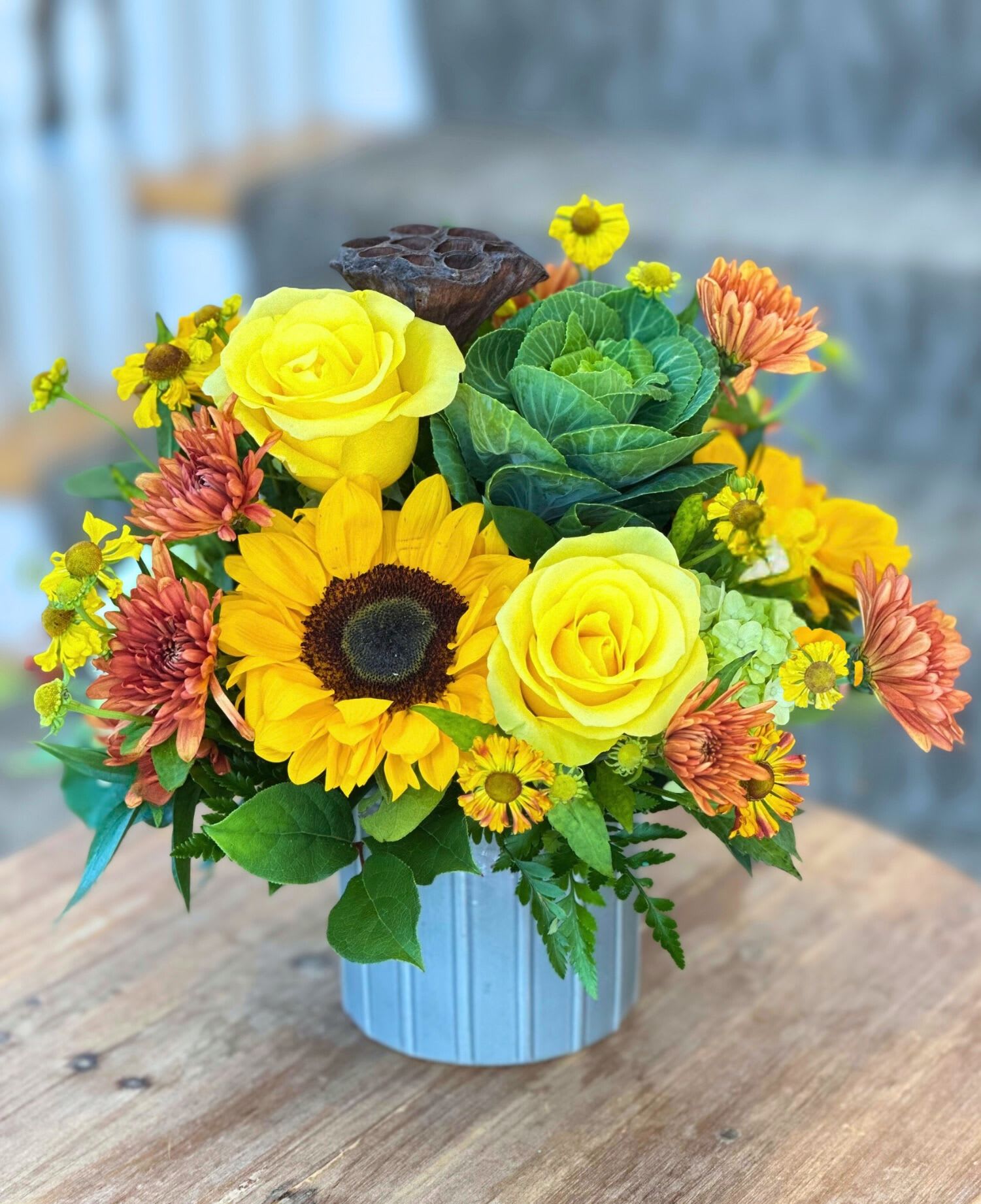 Sunbeam Harvest - FALL COLLECTION | LOCAL DELIVERY ONLY  Celebrate the warmth of fall with this sunflower arrangement that blends earthy autumn tones with rustic charm. This arrangement is styled in a neutral keepsake container (available in green, grey, or cream) and includes sunflowers, green hydrangea, roses, kale, mums, and touches of Helen's flower (sneezeweed). This piece brings seasonal beauty to any space. 