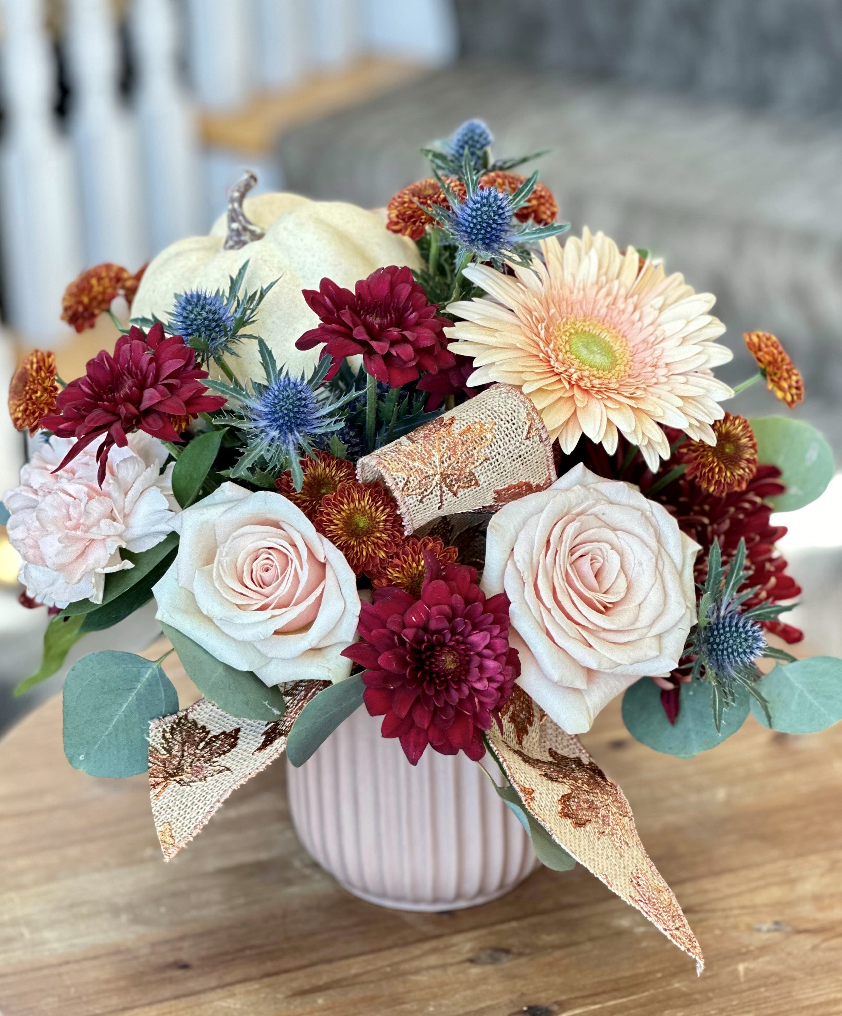 Autumn Blush Bouquet - FALL COLLECTION | LOCAL DELIVERY ONLY  Soft, romantic fall tones come to life in this bouquet of gerbera daisies, mums, thistle, roses, and carnations, finished with seasonal ribbon. Arranged in a ceramic keepsake container that varies in color, blending creams, blush, and burgundy for a warm, elegant touch to any space. 