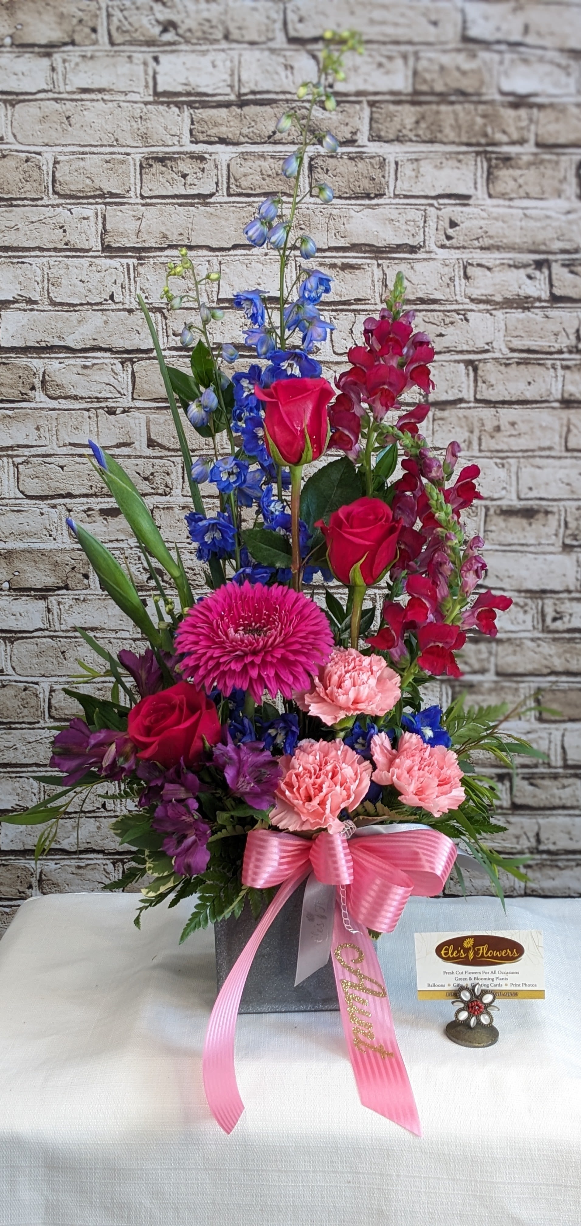 Pink, Blue & Purple Tribute Pink, Blue & Purple Tribute - This elegant sympathy arrangement blends soothing shades of blue, gentle lavender, and soft pink in a tall, narrow design that feels both modern and timeless. Delicately arranged blooms rise in graceful tiers, creating a sense of upward movement and quiet strength. Its non-traditional style offers a unique tribute, symbolizing peace, remembrance, and the enduring beauty of cherished memories.  The designs we create are custom and the blooms and containers will vary. We use the freshest product available to create the perfect floral combination for the recipient! If you have any special requests, please add those in the "special instructions" portion of your order to help us dial in your vision. Otherwise, our skilled designers, Brett & Sara, will take it from here!   Please note that the photos are examples only – floral selection will vary.  Approximate Dimensions: 30"H x 12"W
