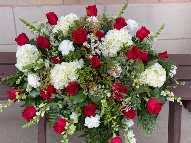 Red & White Tranquility Casket Spray Red & White Tranquility Casket Spray - A dramatic contrast of brilliant red and tranquil white flowers expresses the range of emotions coloring the memorial experience, offering consolation and hope for the future to loved ones, family and friends. This lovely mix of flowers such as red roses, hydrangeas and carnations is balanced by white chrysanthemums and larkspur set against an assortment of greens including eucalyptus, salal, and leatherleaf fern to create a strikingly beautiful casket spray. This is a half casket spray.  Approximate Dimensions 21"H x 39"W