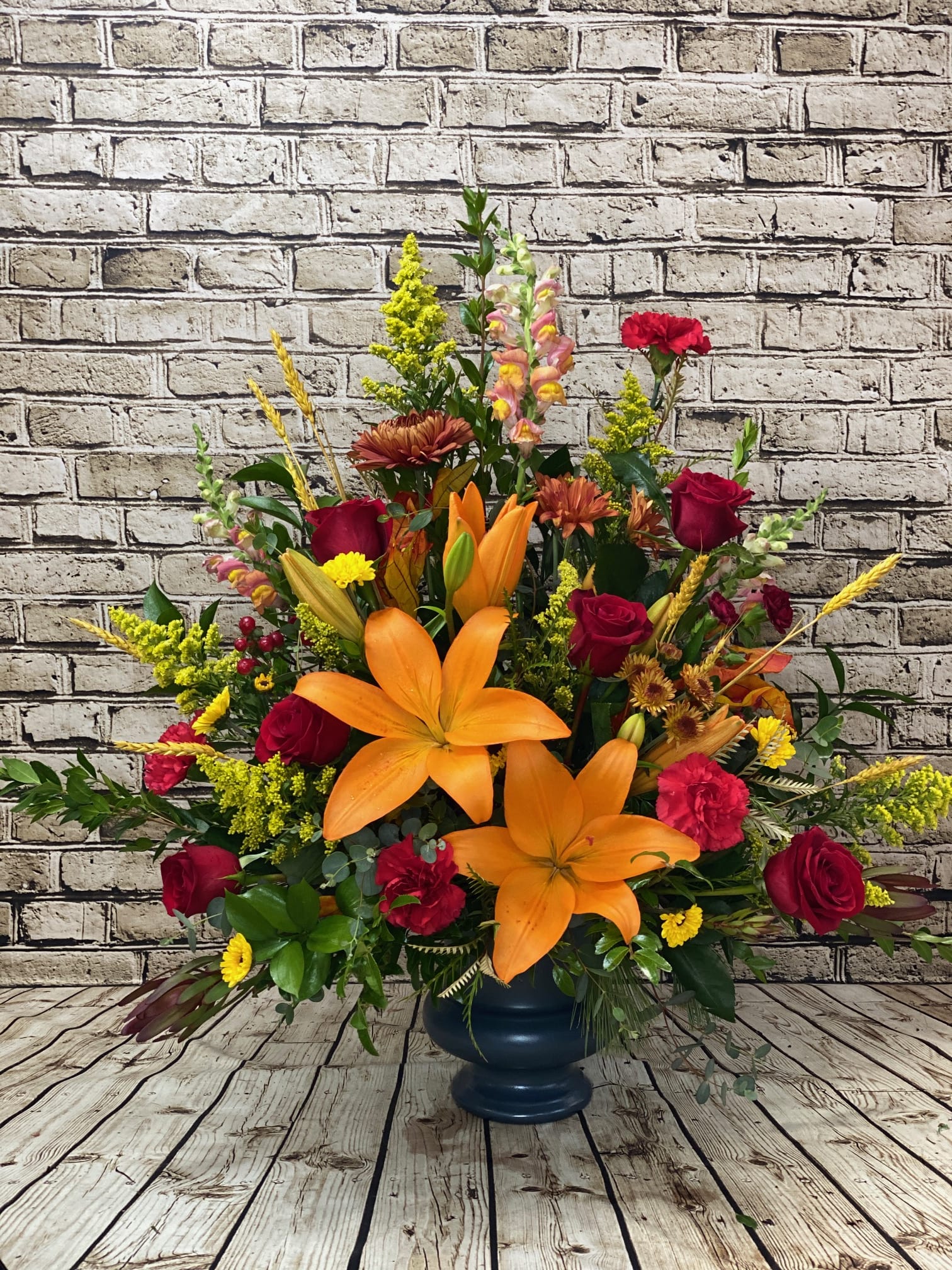 Autumn Memories Traditional Spray Autumn Memories Traditional Spray - This radiant spray brings warmth and comfort to a funeral or memorial service with its rich, vibrant colors. Designed with a striking blend of red roses, orange lilies, rust-colored mums, red carnations, and yellow daisies, this arrangement symbolizes love, remembrance, and the beauty of a life well lived. Lush greenery provides contrast, while the cascade of blooms offers a timeless expression of sympathy and the natural wheat add a touch of nature. Perfect for displaying alongside the casket, this side spray is both traditional and uplifting. Some blooms may vary.   Grand size approximately 36"H x 36"W