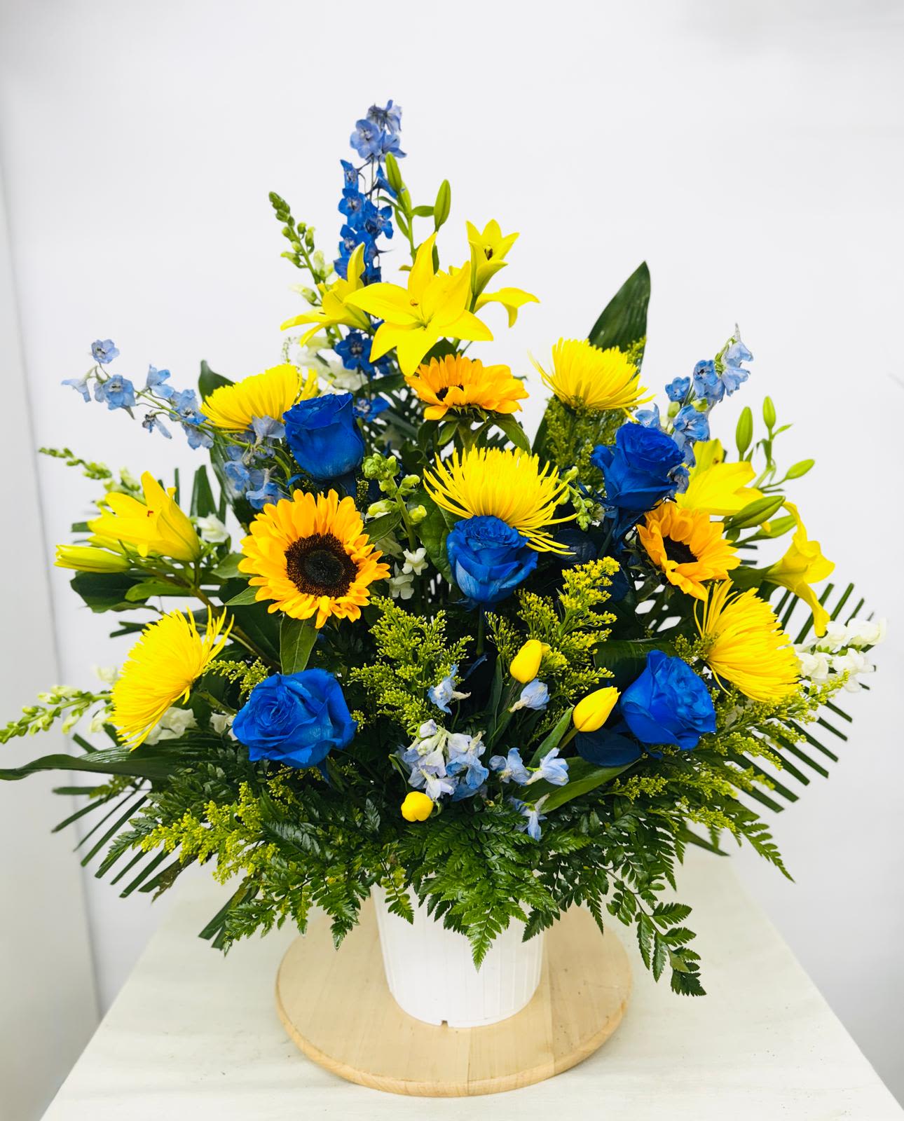 Blue and Gold Basket Tribute Blue and Gold Basket Tribute - Vibrant Blue and Yellow basket includes delphinium, sunflowers, daises, tulips and roses blended with fillers of statice and solidago.