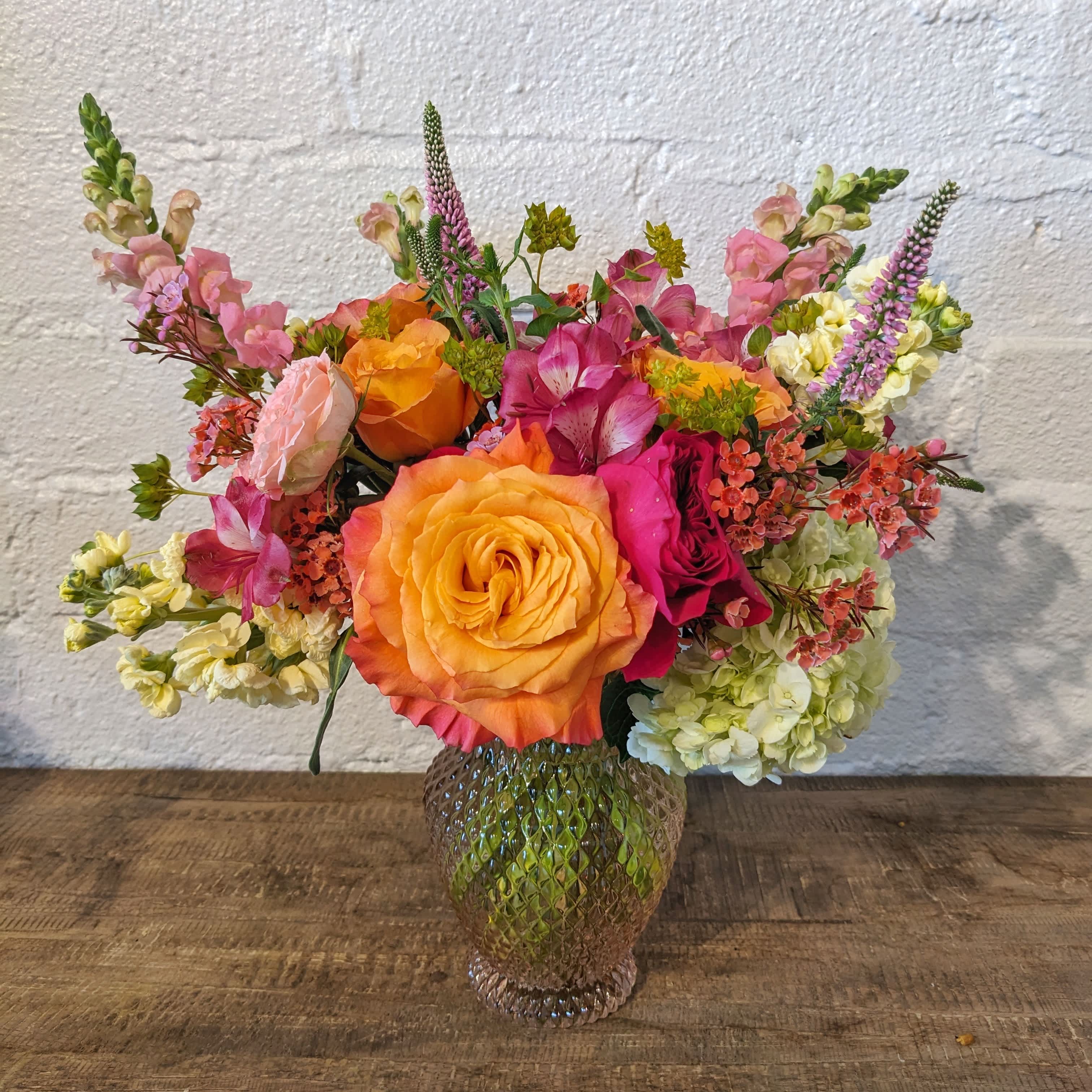 Juicy Blooms  - A vibrant, perfect for summer arrangement. An all around, compact style with some texture, in a peach glass vase. 