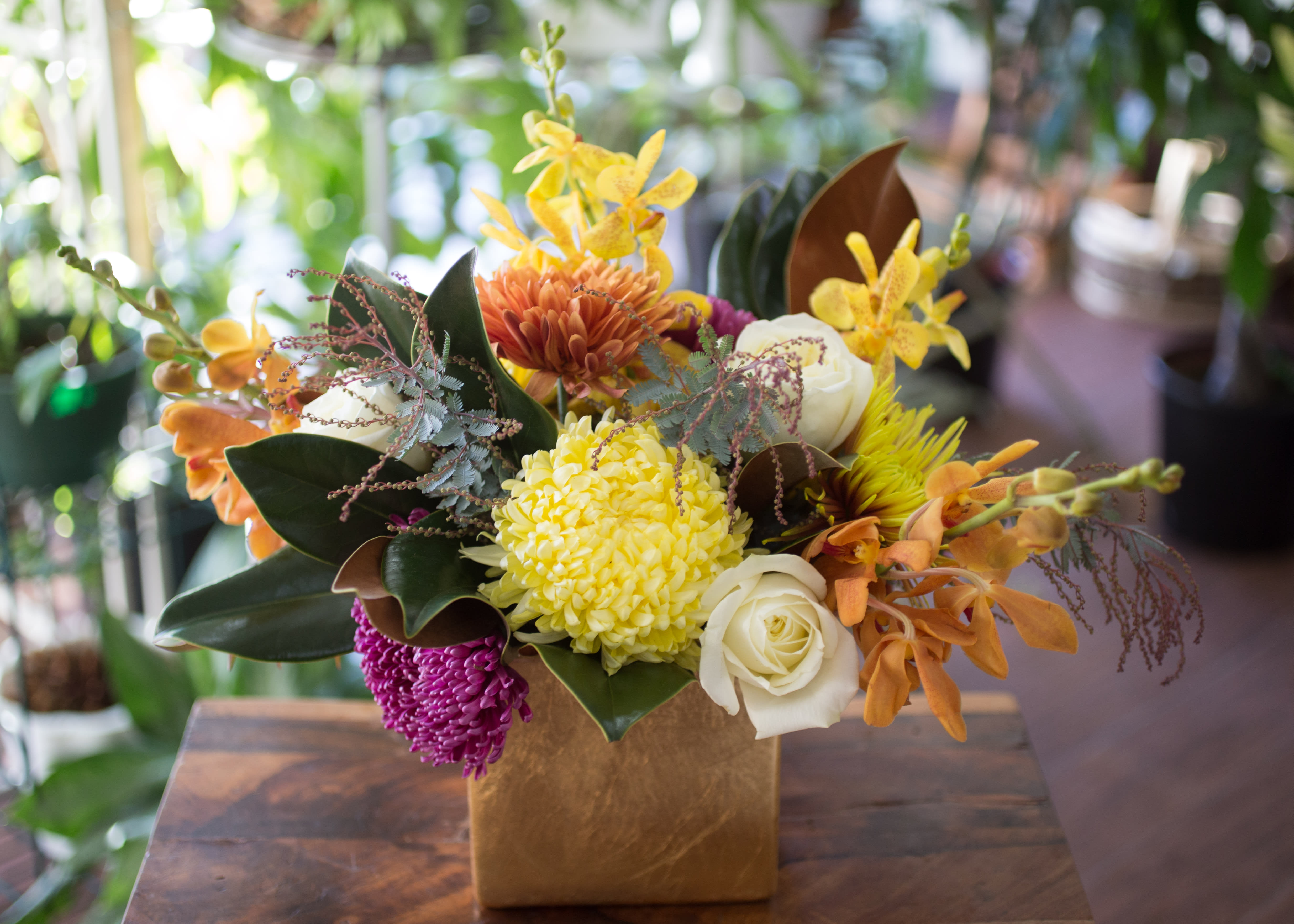 Maggie - Magnolia leaves, Chrysanthemums, Roses and Orchids create the perfect table centerpiece, arranged in a gold ceramic container.