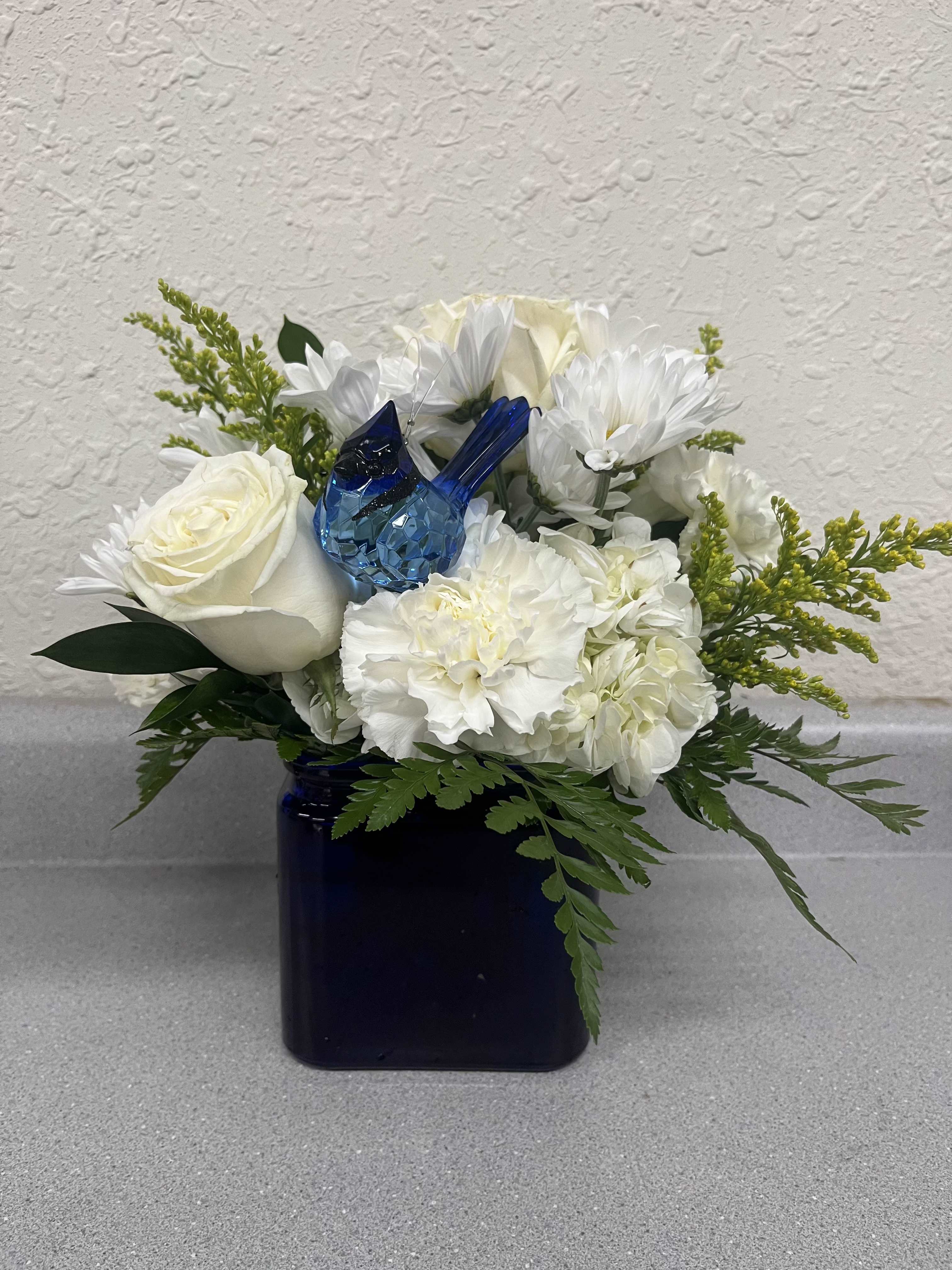 Bluebird of Happiness - Need a little pick me up? This simple and elegant arrangement is perfect for any occasion.  A crystal expressions bluebird is featured in an assortment of white flowers artfully arranged in a cobalt blue vase.
