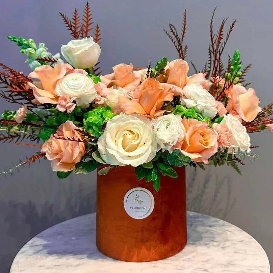 Flower Fairy - Immerse yourself in floral magic with Flower Fairy arrangement. This captivating bouquet brings together lush greenery, fragrant eucalyptus, elegant peony roses, vibrant orange roses, and pristine white roses, all beautifully arranged in a charming corduroy box accented with soft moss. Perfect for adding a touch of whimsy and elegance, let Flower Fairy make your special moments truly magical.