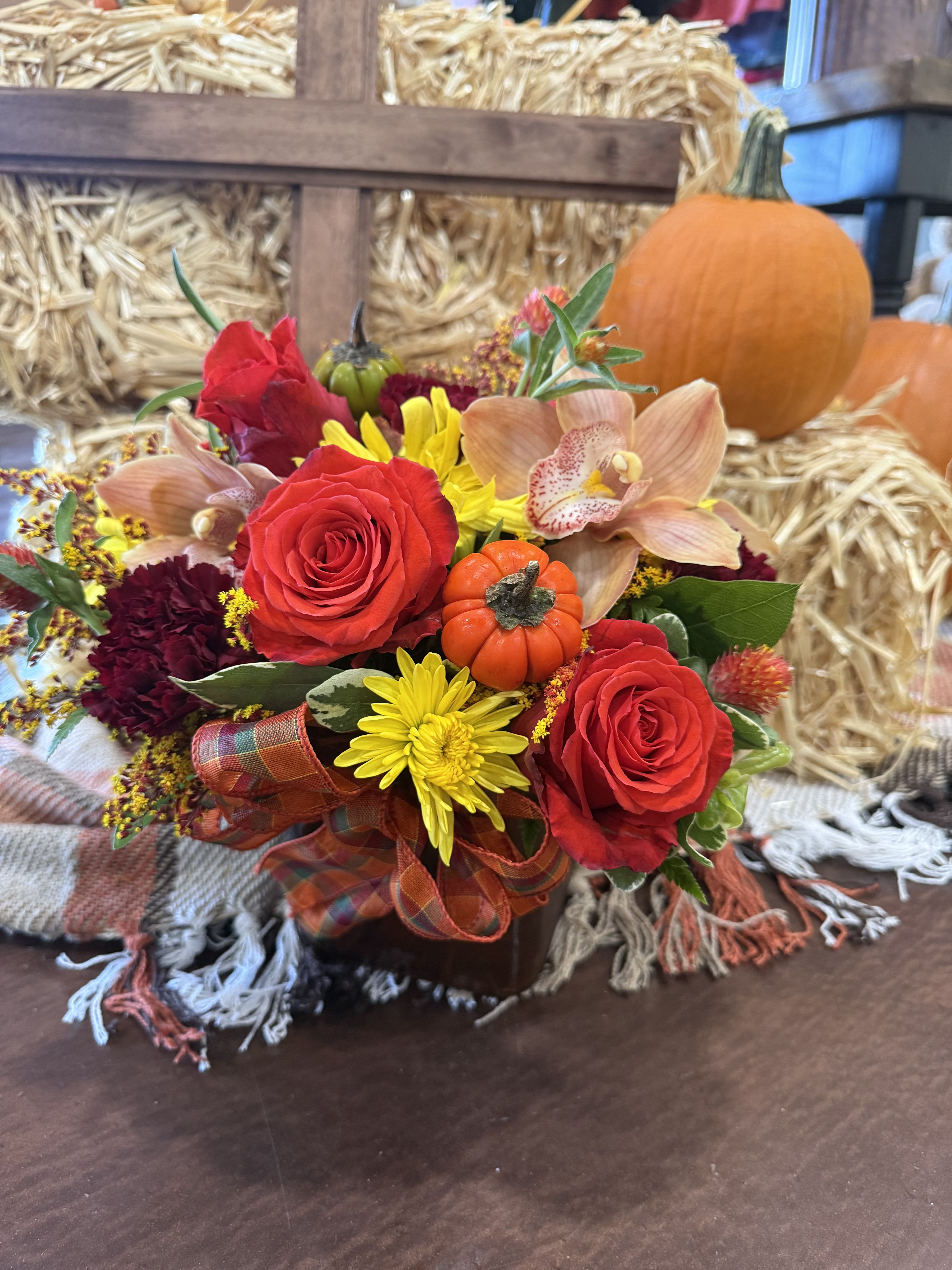 Autumn Meadow  - Brimming with the warmth of autumn, this arrangement features radiant orange roses, golden yellow mums, rich burgundy blooms, and an elegant orchid for a touch of sophistication. At its heart, a miniature pumpkin and festive plaid ribbon capture the spirit of the season. A perfect blend of rustic beauty and cozy elegance, making it an ideal centerpiece for fall gatherings or a thoughtful seasonal gift.