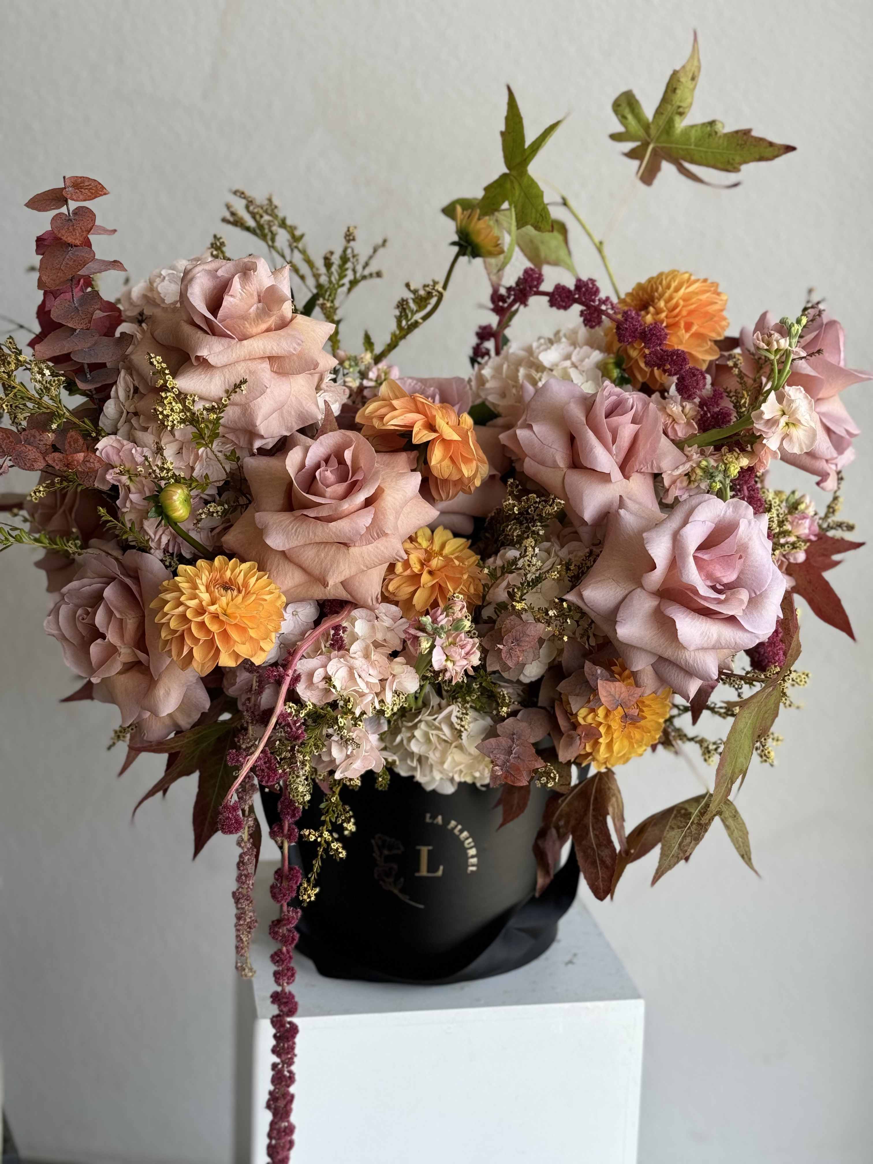 Whispers of Fall Whispers of Fall - Delicately capturing the subtle beauty of autumn, this arrangement combines soft, muted tones with warm, golden accents. Featuring creamy white hydrangeas, fall roses, and orange dahlias, it is complemented by touches of caramel-colored foliage. All carefully arranged in a sleek black box, this design evokes the quiet elegance of the season's changing leaves and crisp air, making it the perfect statement piece for adding a touch of autumn luxury to any space.