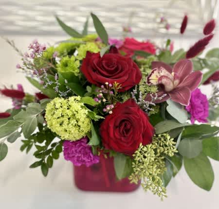 In The Moment In The Moment - Stunning red roses arranged with pink and green blooms, burgundy dried filler, and fresh mixed greenery into a tinted glass vase.
