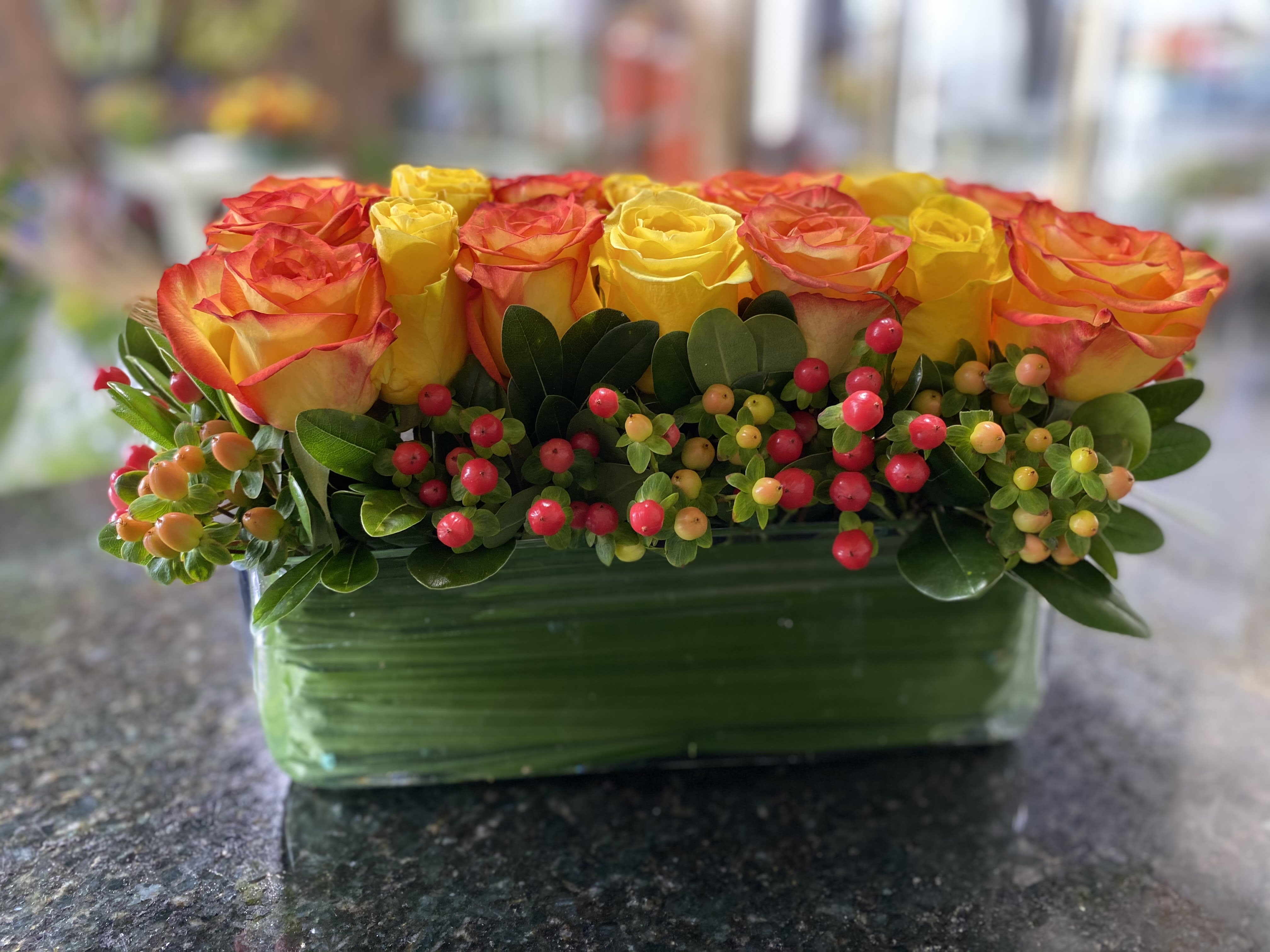  Roses in Rectangle - Table centerpiece arranged in 12 inch X 4 inch rectangle  - Made with 21 red and yellow tone roses - Hypericum and accented with greens. Perfect for the medium size table .  