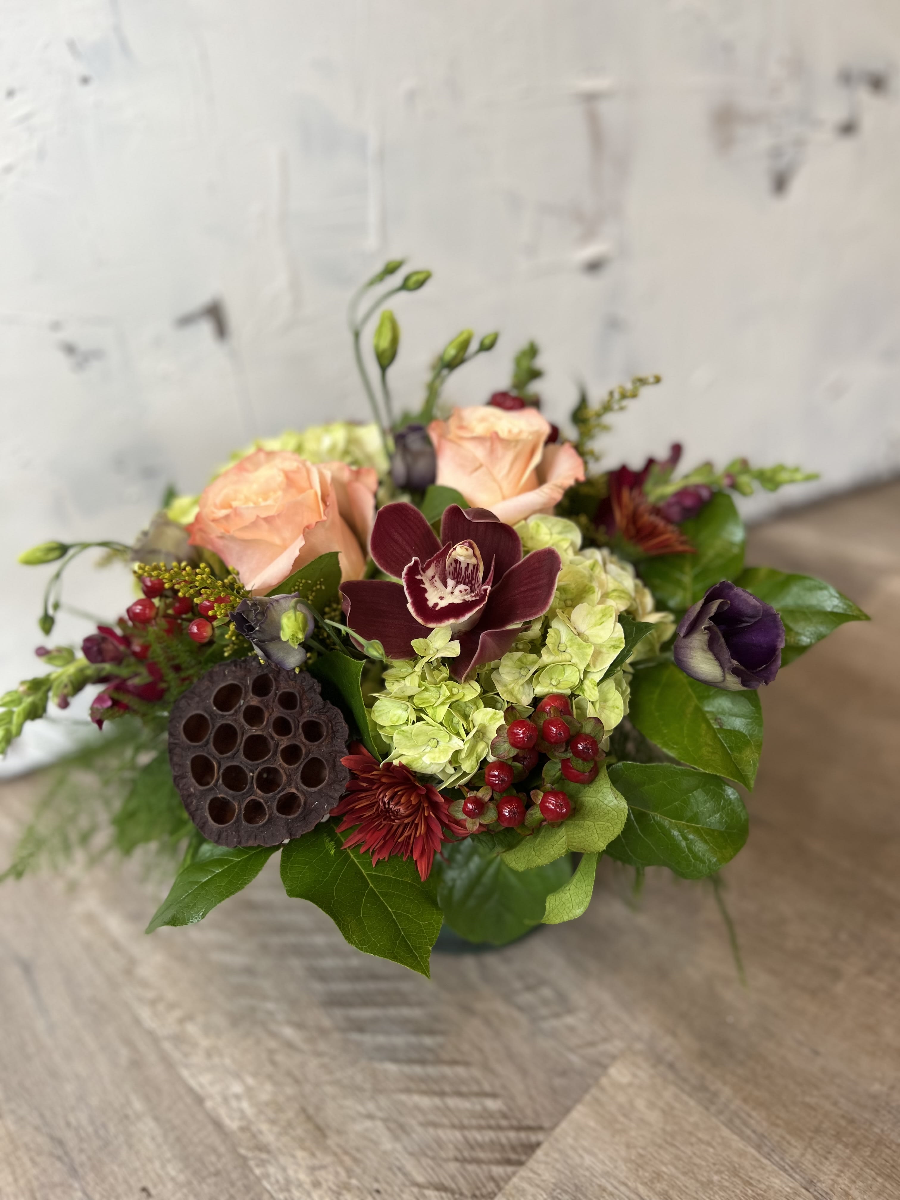 Caramel Apple - This stunning arrangement embodies the rich, luxurious colors of fall.  Deep burgandy orchids stand tall and regal, much like the skin of a delectable caramel apple.  Soft inviting peach roses infuse the arrangement with warmth and elegance.  Green hydrangea brings balance and freshness, just like a crisp fall breeze.  Bring the opulence and beauty of the season into your space with this captivating arrangement!   This arrangement is perfect for adorning smaller spaces or as a charming centerpiece on your dining table.  It makes for a lovely addition to any intimate gathering. 