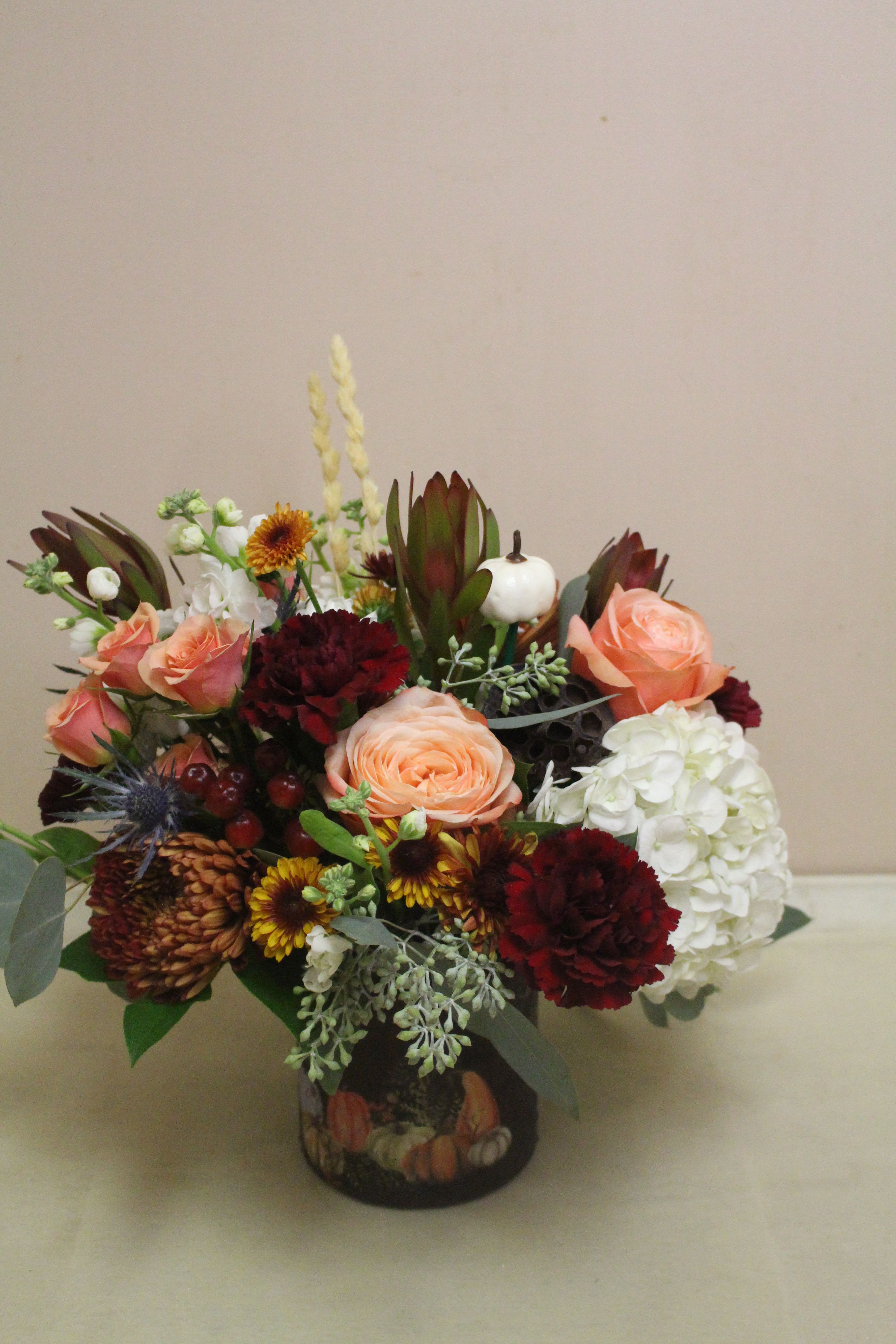 Gourd Garden  - A unique perspective on fall, featuring a vase filled with deep cranberries, soft peaches, and sages. The arrangement is in a deep-colored vase with a pumpkin patch scene.