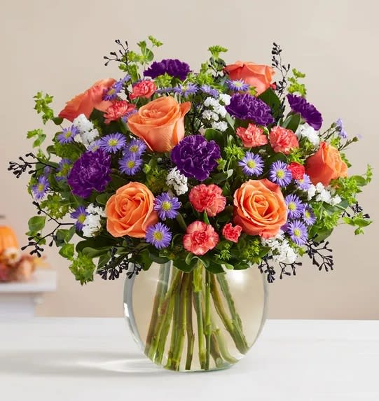 Autumn Delight -  Warm orange roses mix with rich purple carnations for a contrast of color. Lush greenery all around adds texture to this spirited bouquet, capturing everything there is to love about this time of year.