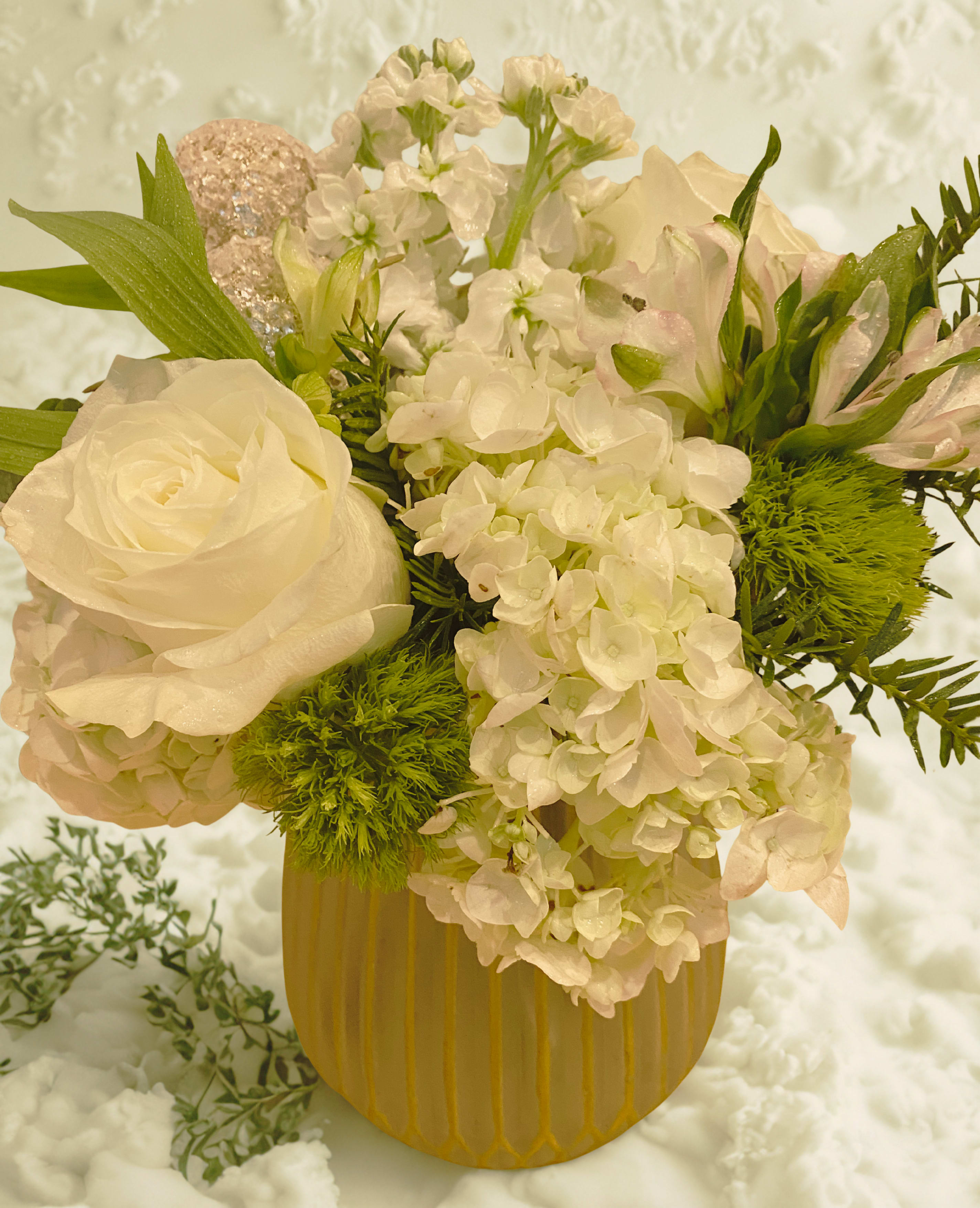 Seasonal Delight Chandra Glass - Who doesn't love the pure elegance of white and gold for a holiday celebration? This bouquet features white roses, green and white hydrangeas, white stock, green trick dianthus, and white alstroemeria. Eucalyptus and pine are used for greenery. Complimented with frosted gold ball ornaments. Container is frosted Chandra glass with gold stripes. Buy the bouquet and or the container as an add on for candle burning. This beautiful glass vase measures 7&quot; tall and 5.5&quot; wide at the widest point. 