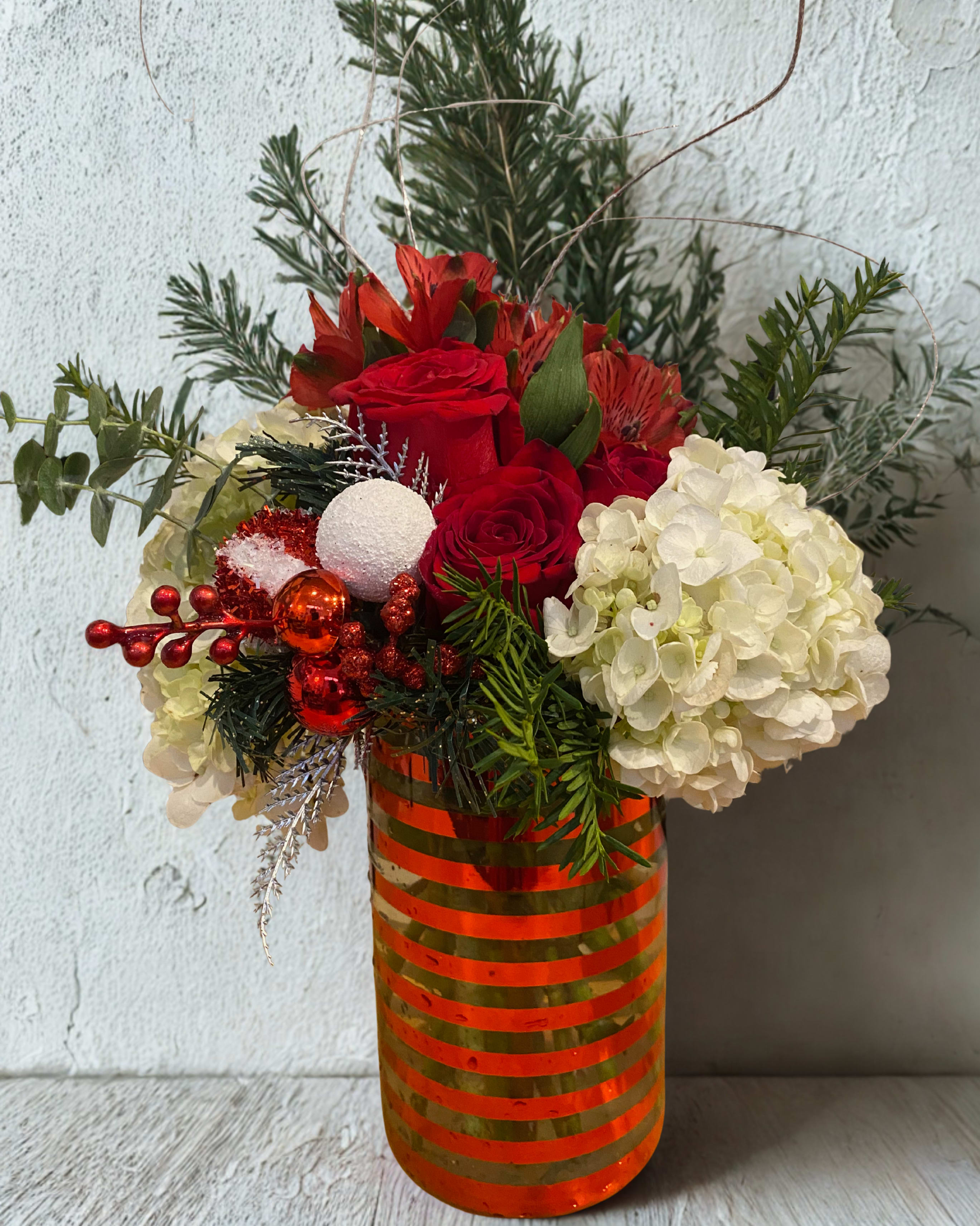 Winter Fun Bouquet - Red alstroemeria white hydrangeas, red roses, pine greens, silver ting ting, red and white/red package ornament, eucalyptus all arranged in a glass keepsake vase with red stripes. Vase is 8&quot; tall X 4.5&quot; wide. Flower arrangement is 14&quot; tall. Substantial in size and a stunning presentation. 