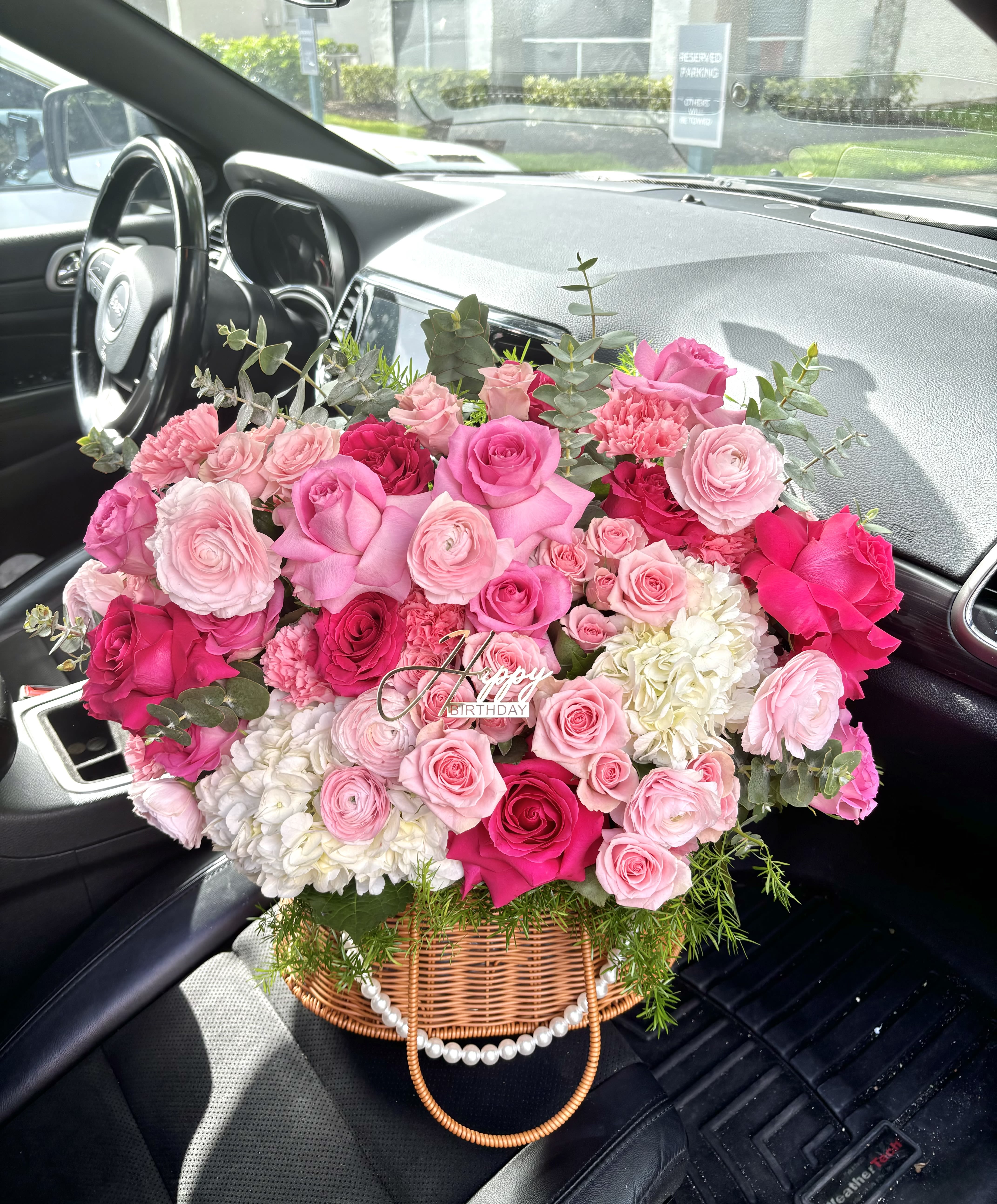 Blushing Elegance Floral Birthday Basket Arrangement - Delight in the luxurious beauty of our “Blushing Elegance” floral basket, an enchanting mix of premium roses, ranunculus, carnations, hydrangeas, and eucalyptus foliage. Presented in a chic wicker basket adorned with a pearl-accented handle, this vibrant bouquet features a harmonious blend of soft blush, creamy ivory, and bold hot pink blooms—perfectly arranged to convey love, celebration, and heartfelt wishes. Whether it’s a birthday, anniversary, or a thoughtful surprise, this arrangement brings timeless charm and joy to any occasion.